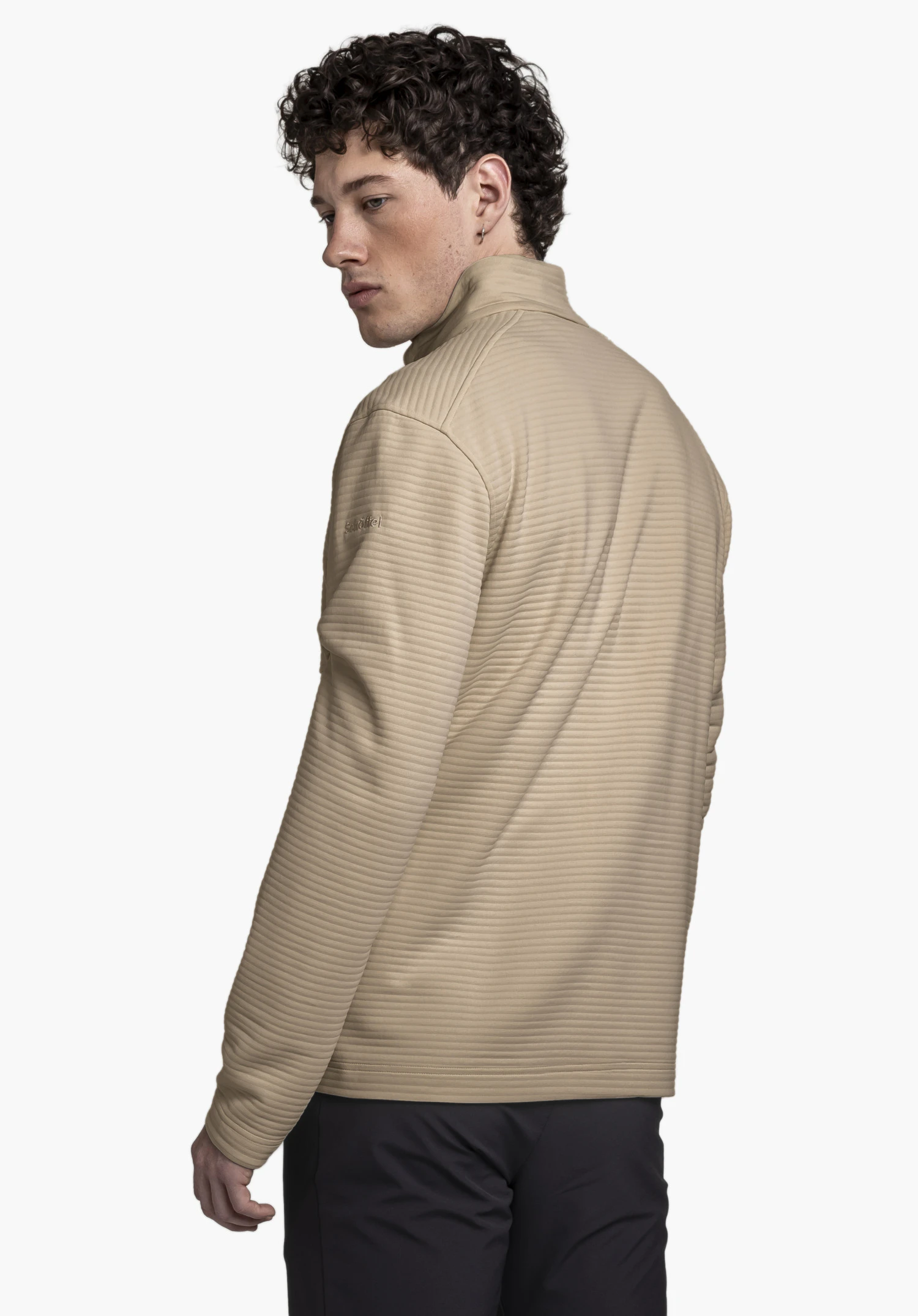 CIRC Fleece Jk Style Smue MNS portée par un mannequin vu de dos, regardant par-dessus son épaule gauche. La veste beige présente une fine texture côtelée et le logo Schöffel sur la manche gauche sur un fond neutre.