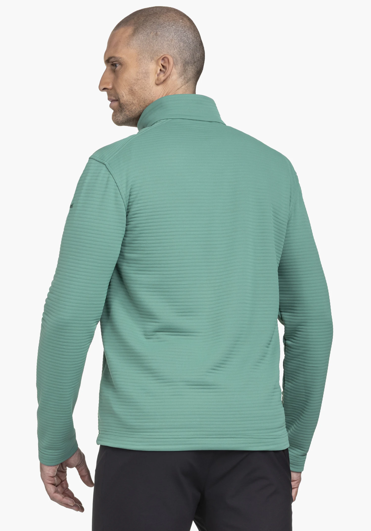 CIRC Fleece Jk Style Smue MNS in Grün. Das männliche Model wird in der Rückenansicht gezeigt und trägt die strukturierte Fleecejacke, auf deren linkem Ärmel das Schöffel-Logo dezent sichtbar ist. Er steht entspannt vor einem neutralen Hintergrund.