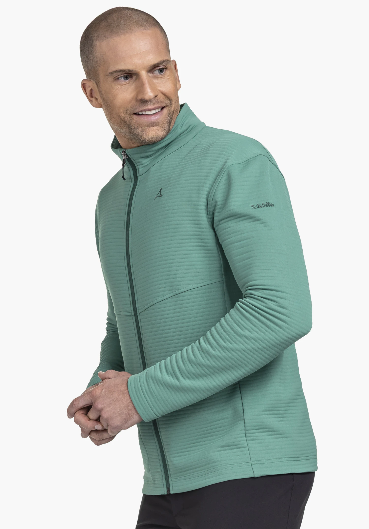 CIRC Fleece Jk Style Smue MNS: Das Model steht seitlich in einer aktiven Pose vor einem neutralen Hintergrund und trägt die Fleecejacke in Grün. Das dezente Schöffel-Logo ist im Brustbereich sowie am Oberarm deutlich sichtbar.