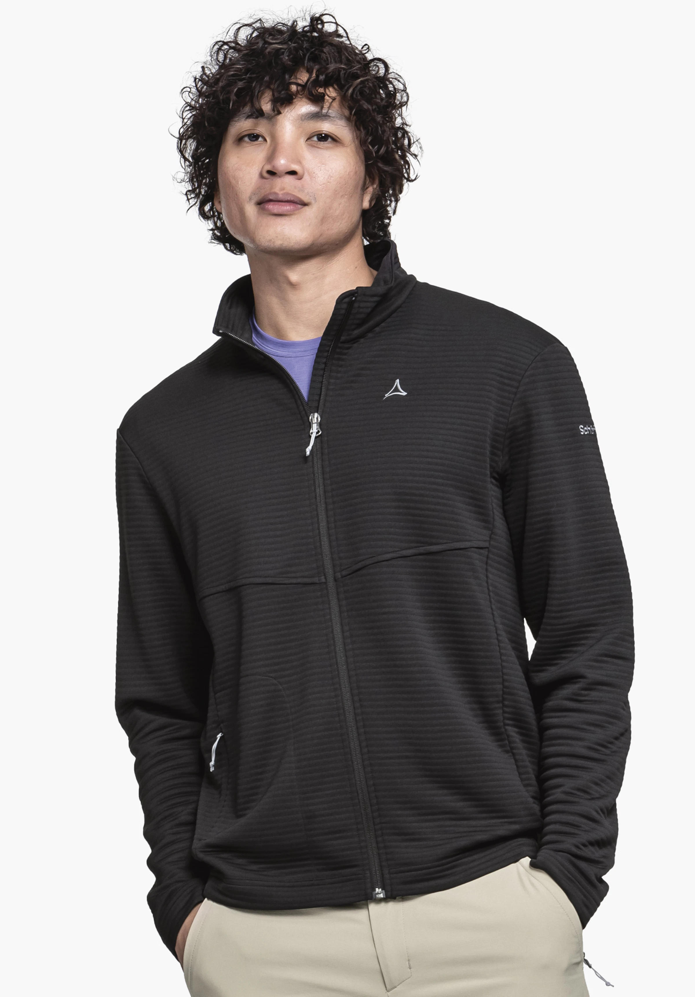 CIRC Fleece Jk Style Smue MNS sur un mannequin se tenant de face avec les mains dans les poches. La veste polaire en noir présente le Schöffel-Logo sur la poitrine et la manche gauche, présentée sur un fond neutre.