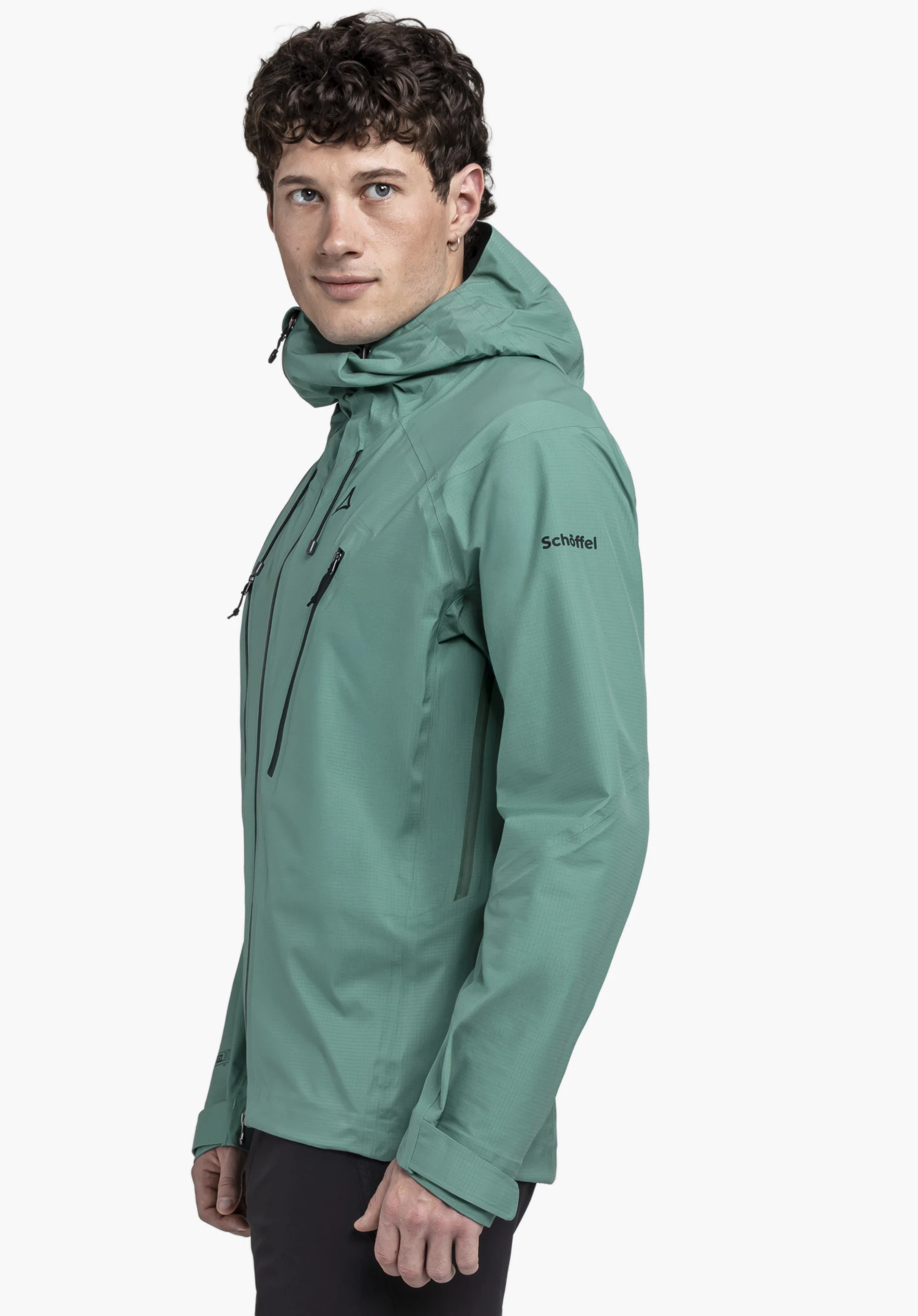 Jacket Style Blaueis MNS in green: A model stands in a side-profile view against a neutral background. The jacket is presented in a modern green tone, with the black Schöffel logo clearly visible on the upper arm, highlighting its premium quality.