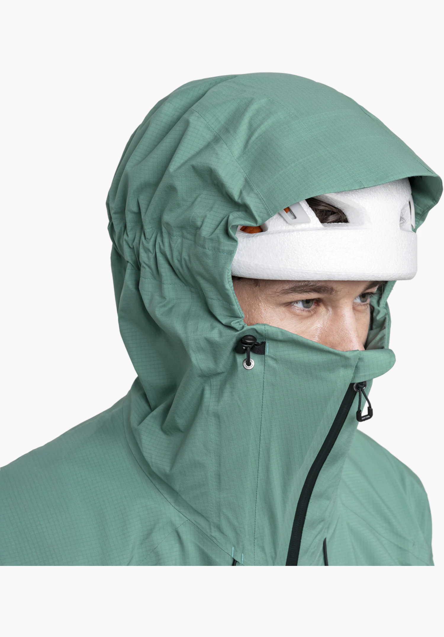 Jacket Style Blaueis MNS shows the detail of the green, helmet-compatible hood with a high-cut face guard, fine ripstop texture and adjustable drawcord over a helmet as a close-up against a white/neutral background.