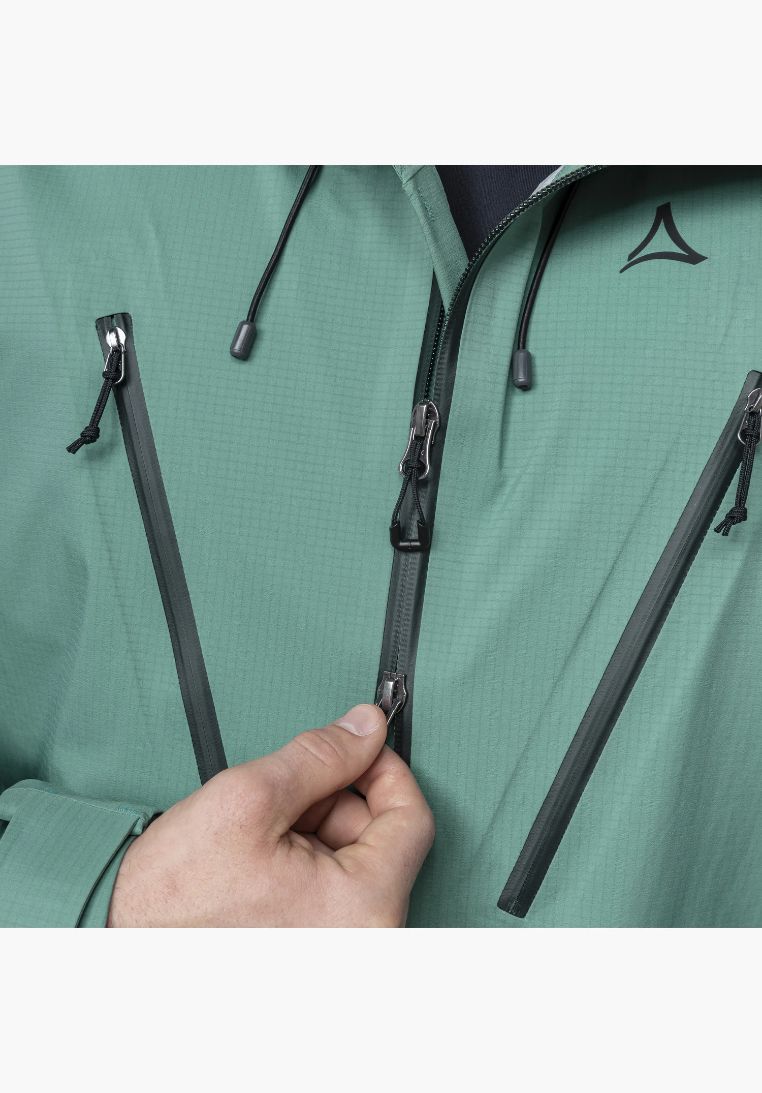Jacket Style Blaueis MNS, detailing the central two-way zip, the angled pocket zips on the green fabric and the Schöffel-Logo, while a hand operates the lower zip. Close-up against a neutral background.
