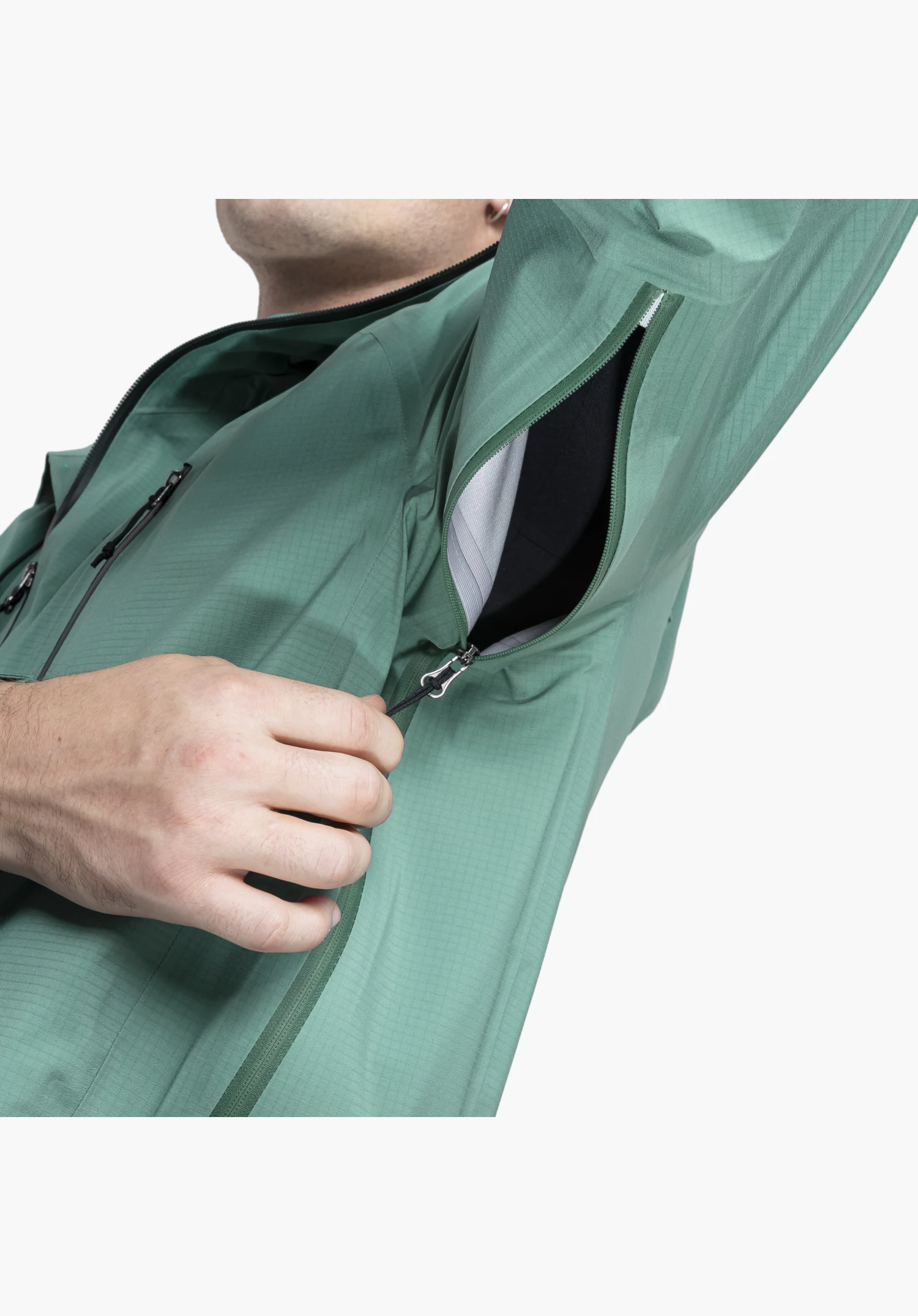 Jacket Style Blaueis MNS, detail view of the opened underarm ventilation zip on the green fabric, operated by a hand, close-up against a white/neutral background.