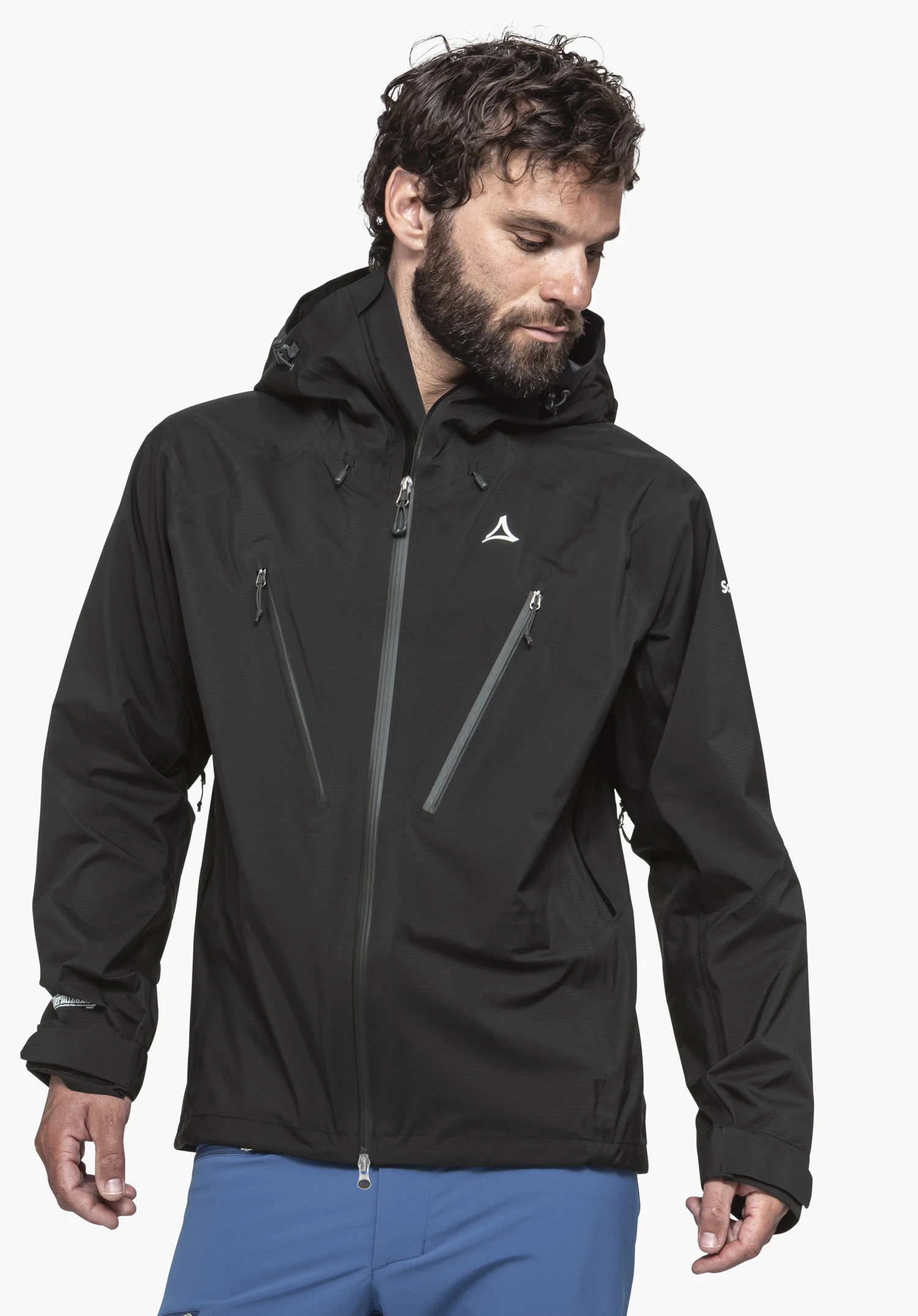 Jacket Style Blaueis MNS schwarze Regenjacke (Schöffel-Logo auf der Brust) trägt ein Mann, der nach unten blickt; diagonale Reißverschlüsse, Kapuze aufgesetzt, vor weißem Hintergrund. Text: Schöffel; GORE‑TEX.