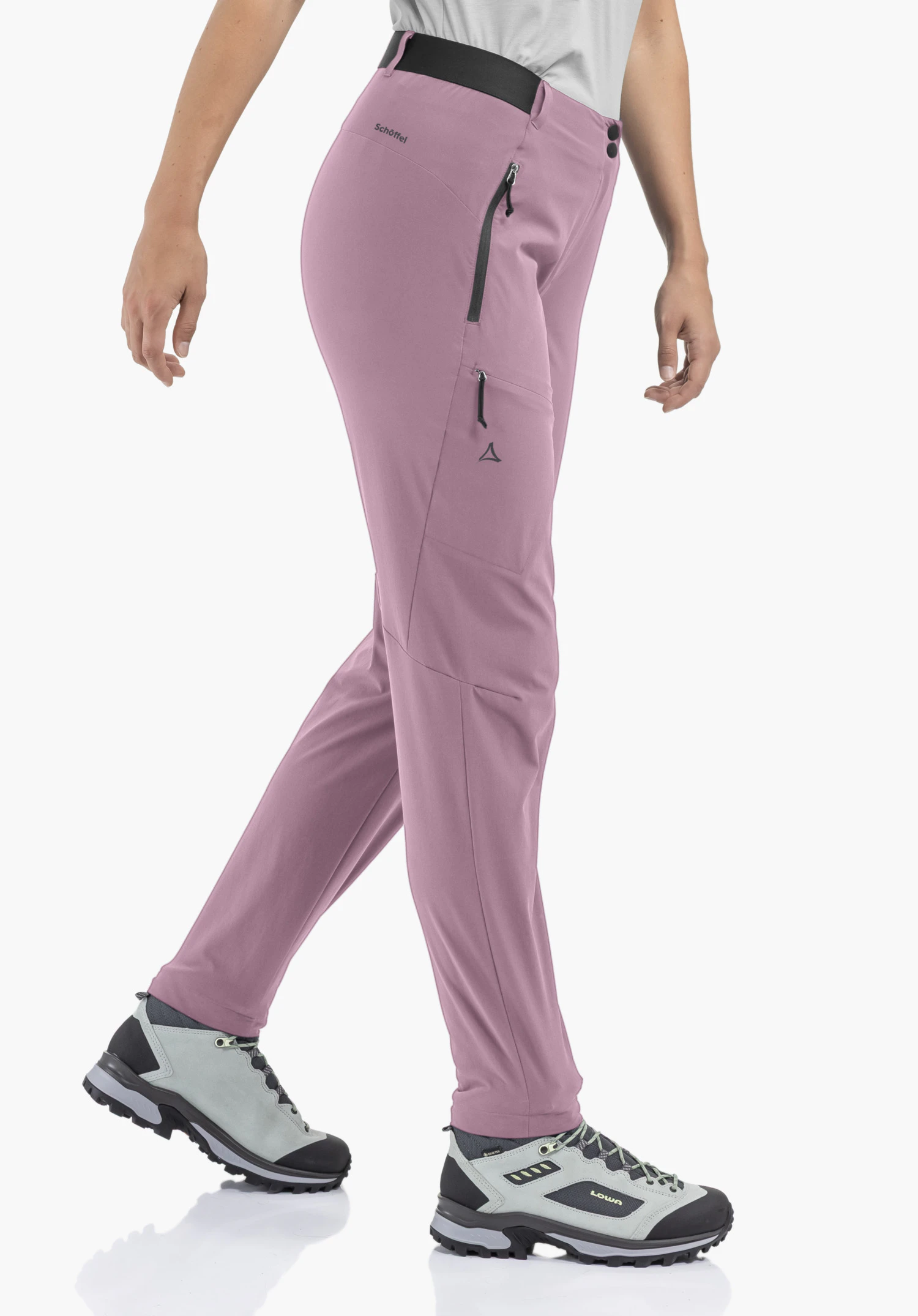 Pants Style Blaustein WMS sur un mannequin qui se tient de profil dans une posture de marche. Le pantalon en rosa présente des poches latérales zippées et le logo Schöffel noir sur la cuisse, photographié sur un fond neutre.
