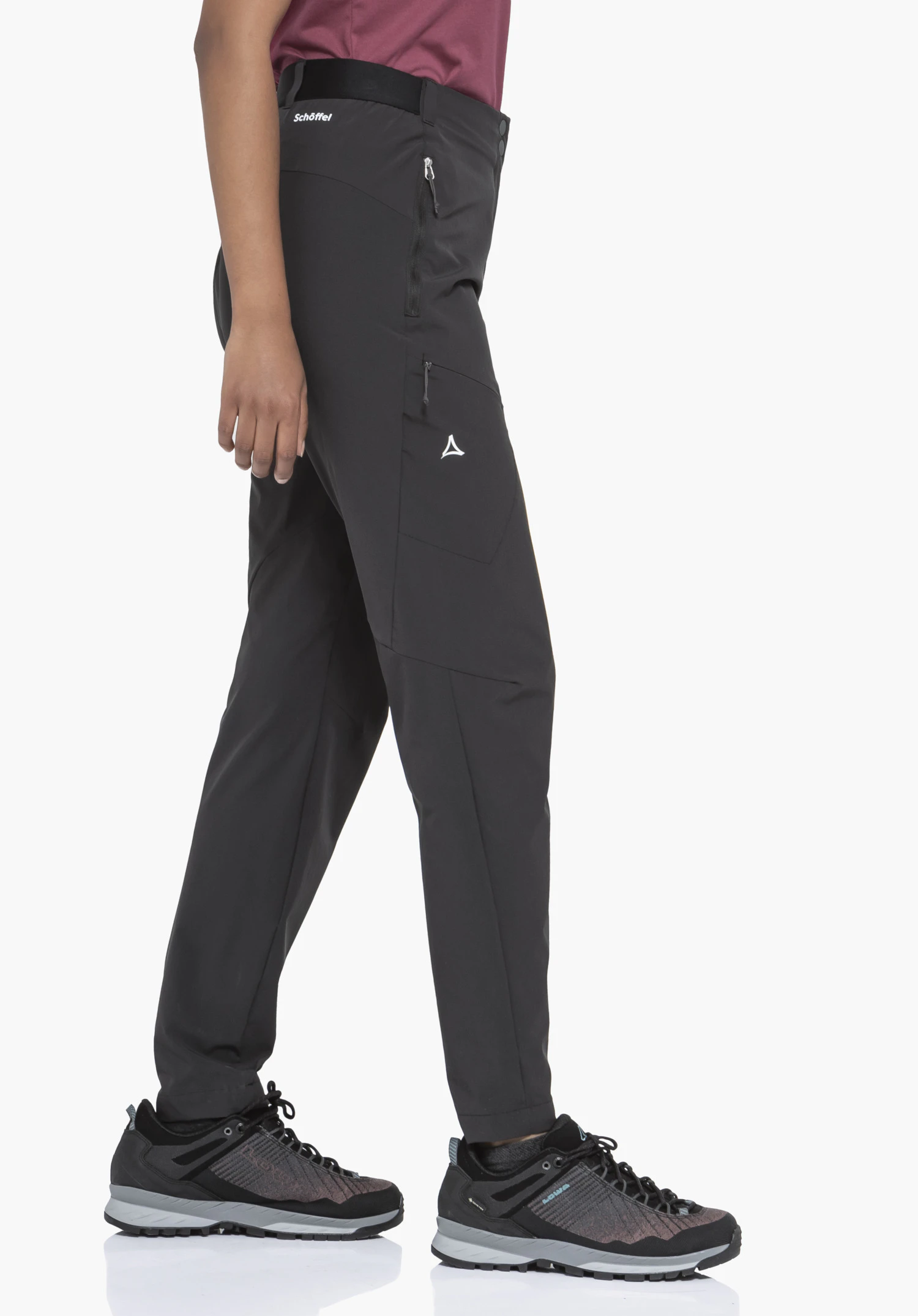 Pants Style Blaustein WMS an einem Model in der Seitenansicht. Die schwarze Hose zeigt sich mit seitlichen Reißverschlusstaschen und dem weißen Schöffel-Logo am Oberschenkel sowie unterhalb des Bundes. Das Model steht in Wanderbekleidung vor einem neutralen Hintergrund.