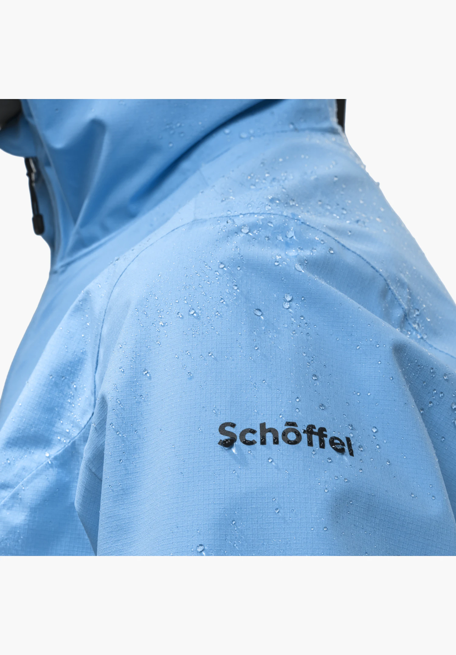 Jacket Style Migandi WMS präsentiert das schwarze Schöffel-Logo auf dem wasserabweisenden, blauen Stoff mit abperlenden Wassertropfen. Nahaufnahme vor weißem Hintergrund.