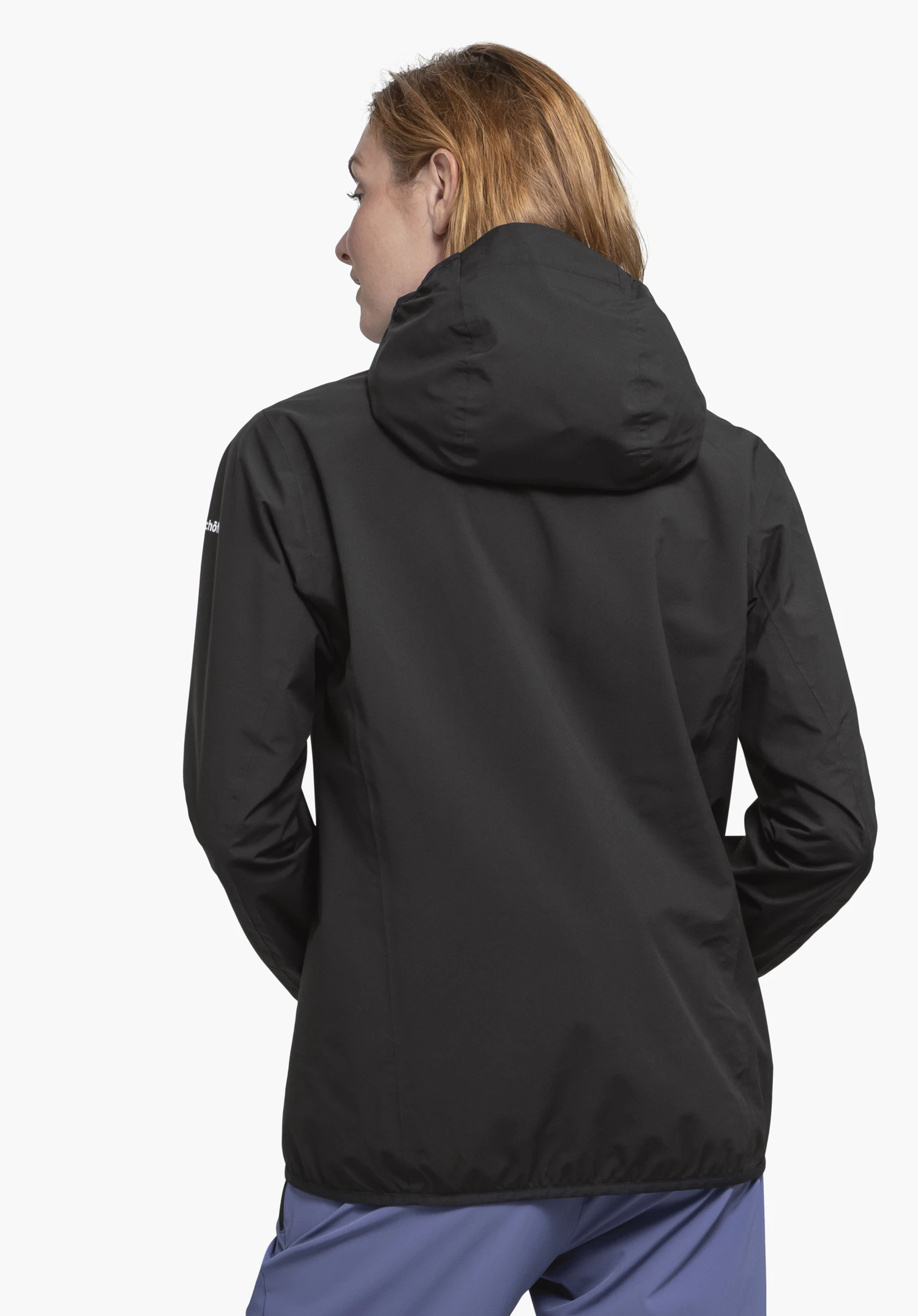 Jacket Style Migandi WMS schwarze Kapuzenjacke, getragen von einer Person mit orange Haaren, steht mit dem Rücken zur Kamera vor neutralem weißem Hintergrund; hellblaue Hose.