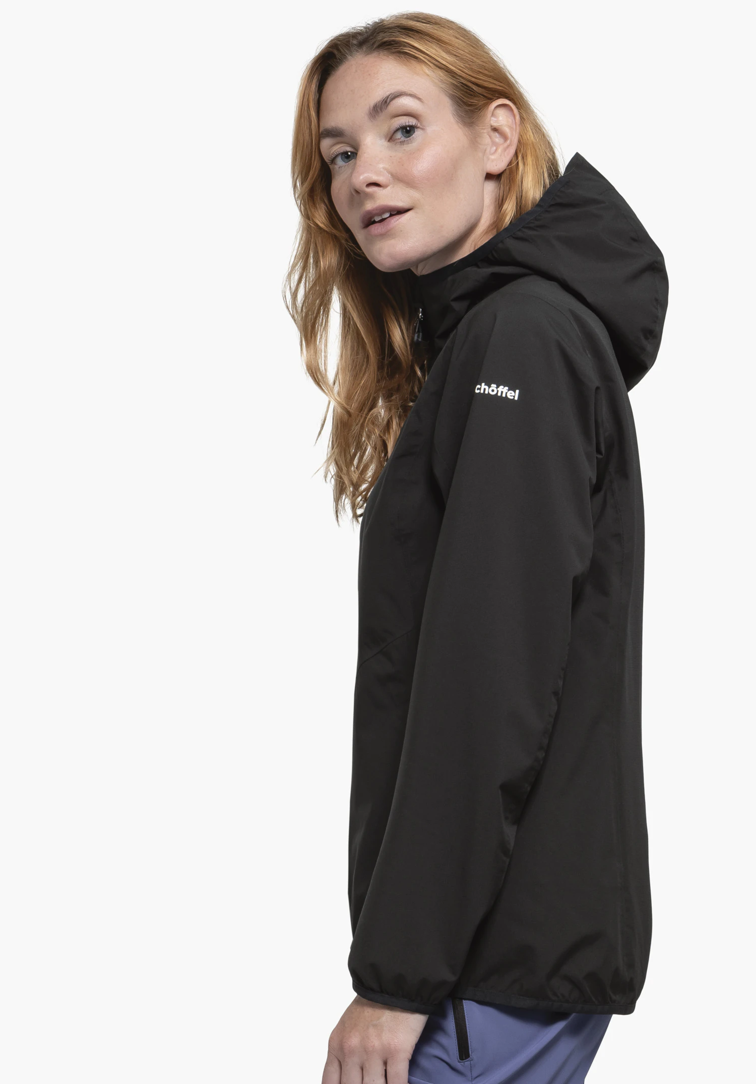 Jacket Style Migandi WMS schwarze Jacke (Kapuze), getragen von Frau, die seitlich blickt; hell gelbes Haar, hell blau Hose; neutraler weißer Studiohintergrund. Text auf Ärmel: "chöffel".