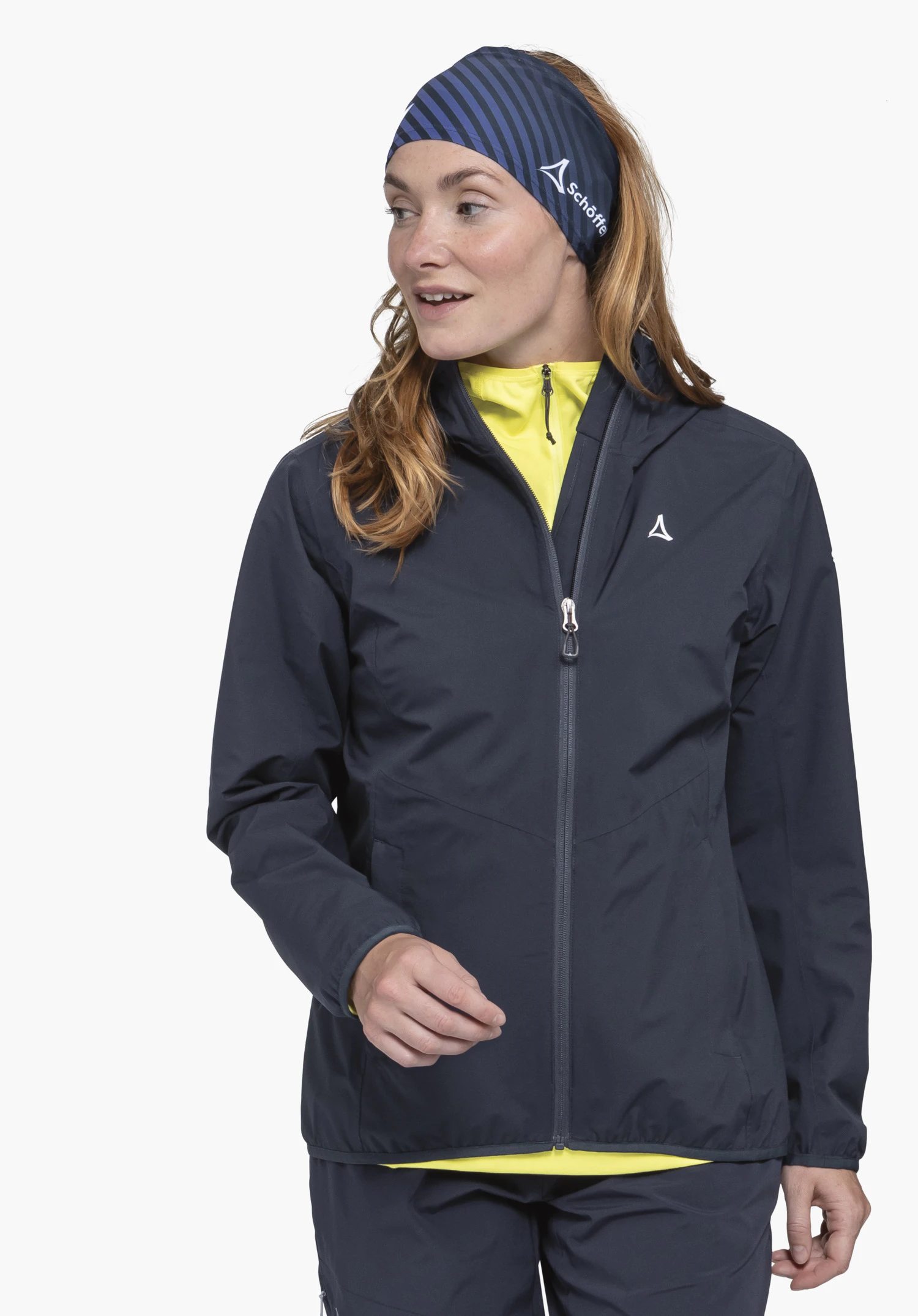 Jacket Style Migandi WMS on a model standing slightly to the side. The jacket in the colour blue features the visible Schöffel-Logo on the left chest and is presented against a neutral background.
