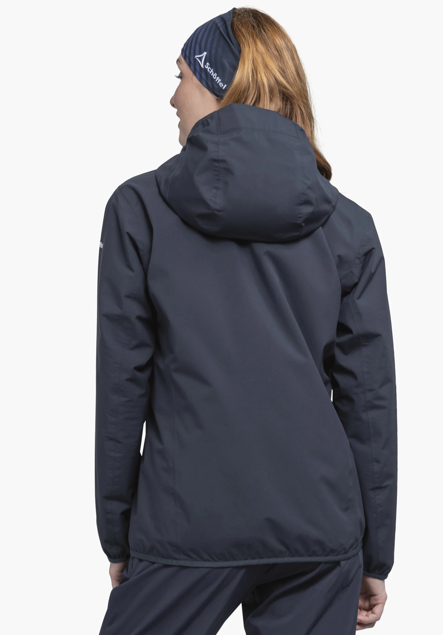 Jacket Style Migandi WMS portée par un mannequin vue de dos. La veste bleue à capuche est associée à un bandeau assorti sur lequel le logo Schöffel blanc est bien visible. La tenue est présentée sur un fond neutre.