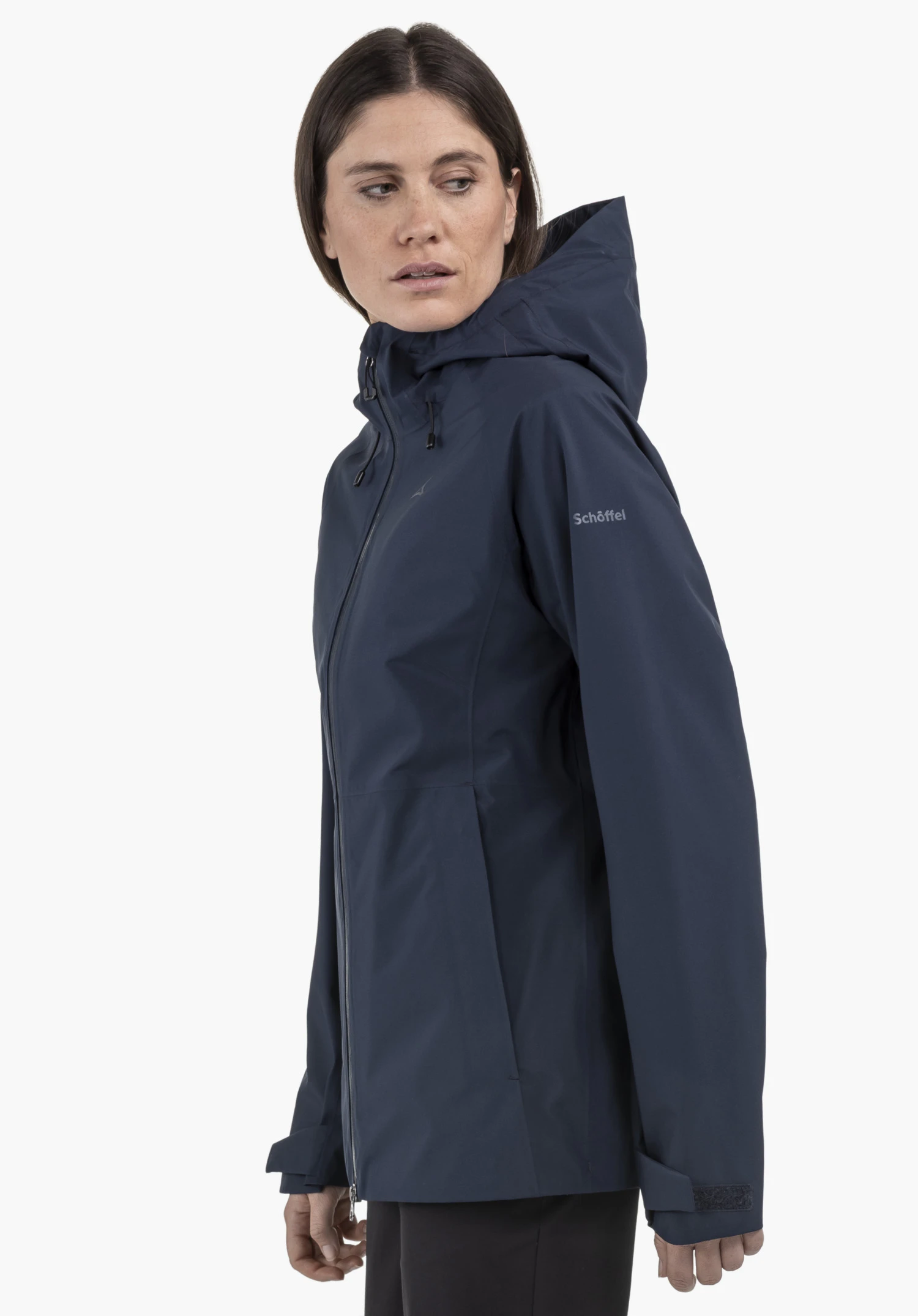 Jacket Style Mauku WMS. A woman is standing sideways in front of a neutral background, wearing the jacket in blue. The subtle Schöffel logo on the upper arm is clearly visible.