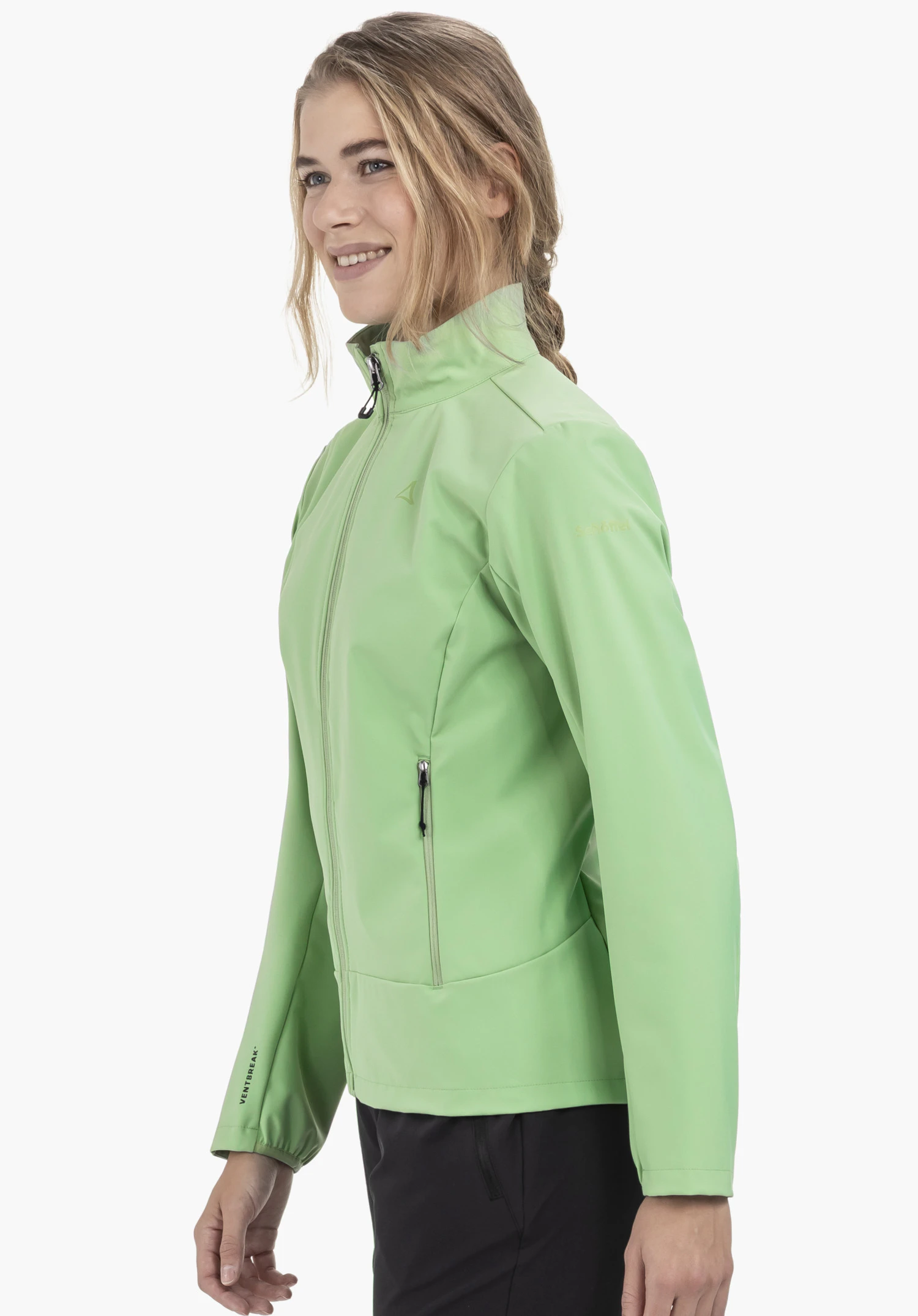 Softshell Jk Style Mirusha WMS in Grün: Eine lächelnde Frau steht seitlich vor einem neutralen Hintergrund und präsentiert die Jacke, wobei das subtile Schöffel-Logo auf der Brust sichtbar ist.