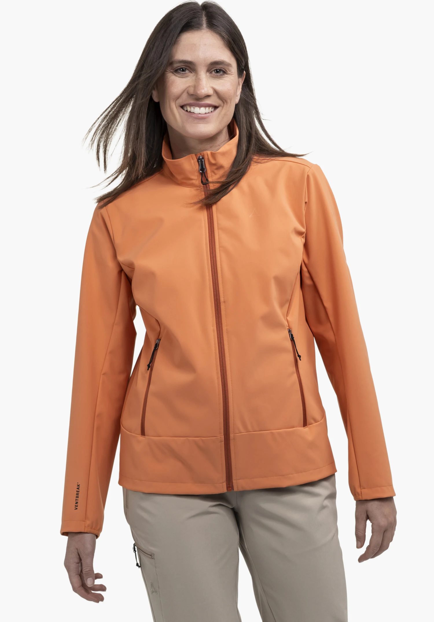 Softshell Jk Style Mirusha WMS in orange. A smiling model stands facing the camera, presenting the jacket with a closed zip and a subtle Schöffel-Logo on the left chest against a neutral background.