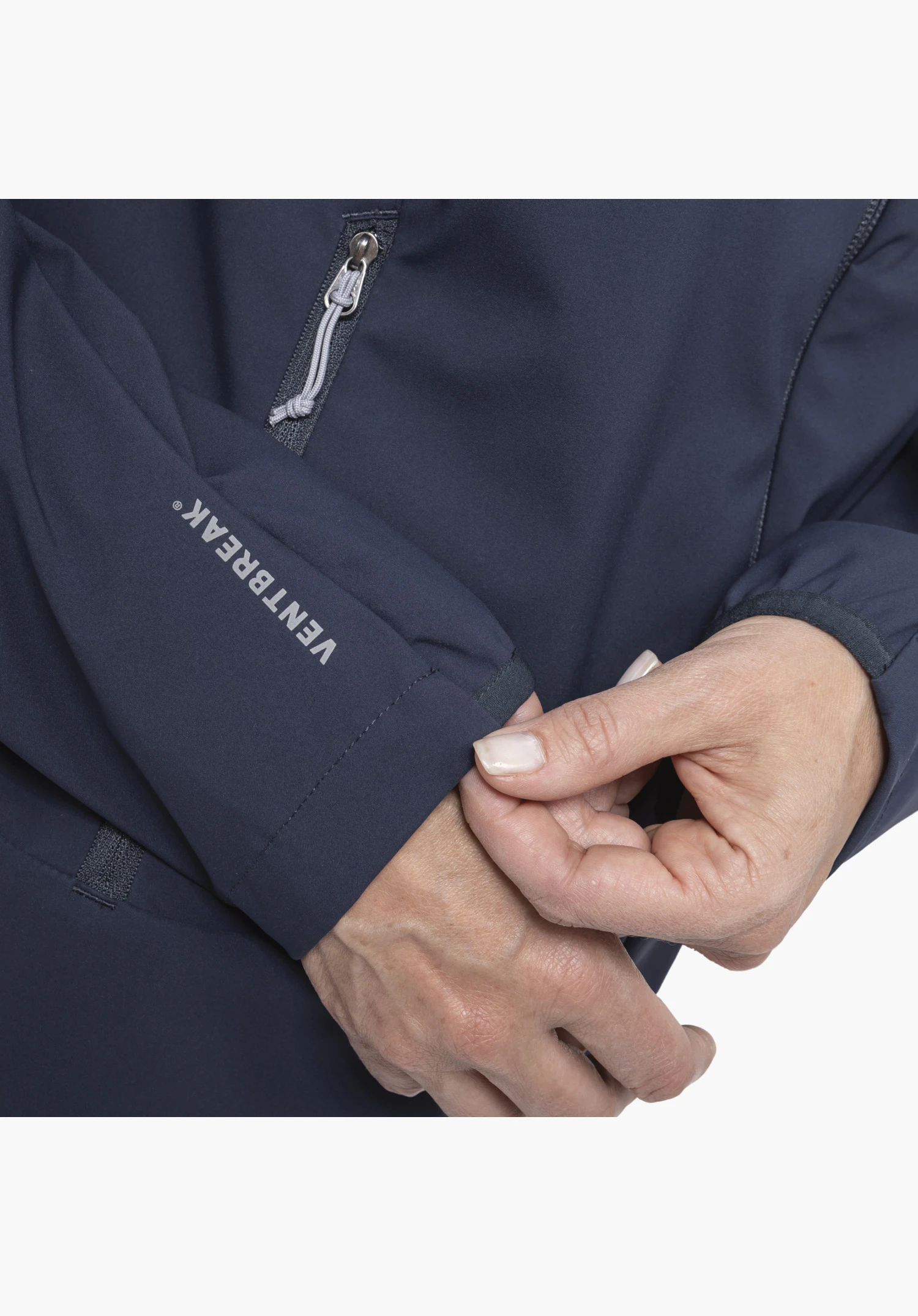Softshell Jk Style Mirusha WMS in het blauw. De detailweergave toont de mouwboord met het VENTBREAK®-opschrift en een ritssluiting met een grijs trekkoord, terwijl handen de stof aanraken. Close-up voor een witte/neutrale achtergrond.