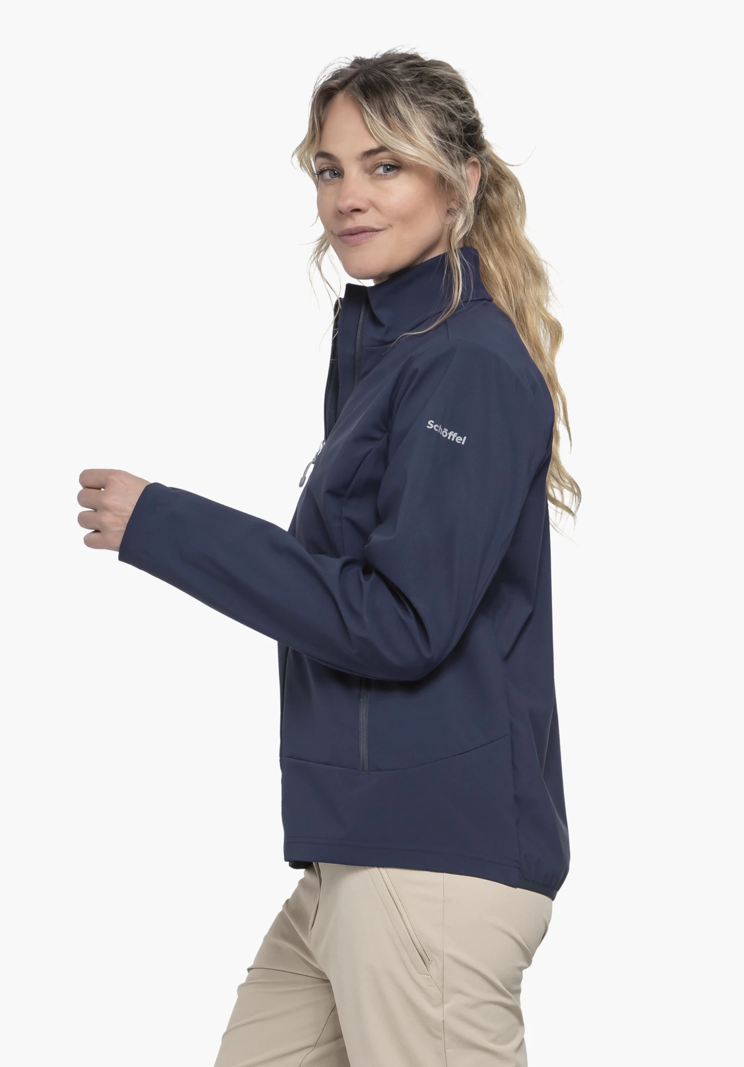 Softshell Jk Style Mirusha WMS in blauw. De atlete staat zijdelings voor een neutrale achtergrond en draagt het jack, waarbij het witte Schöffel-logo op de bovenarm duidelijk zichtbaar is.