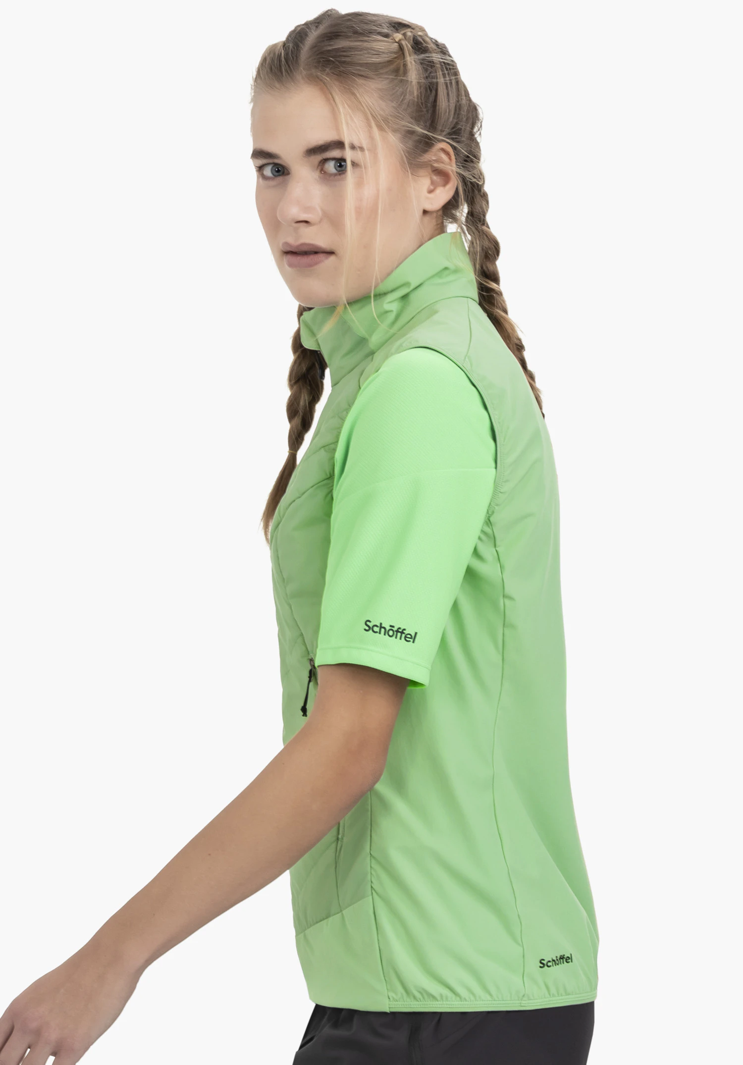 Hybrid Vt Style Blaueis WMS. Un mannequin se tient de profil devant un fond neutre et porte le gilet à manches courtes en vert. Le Schöffel-Logo est clairement visible sur la manche et sur l'ourlet inférieur.