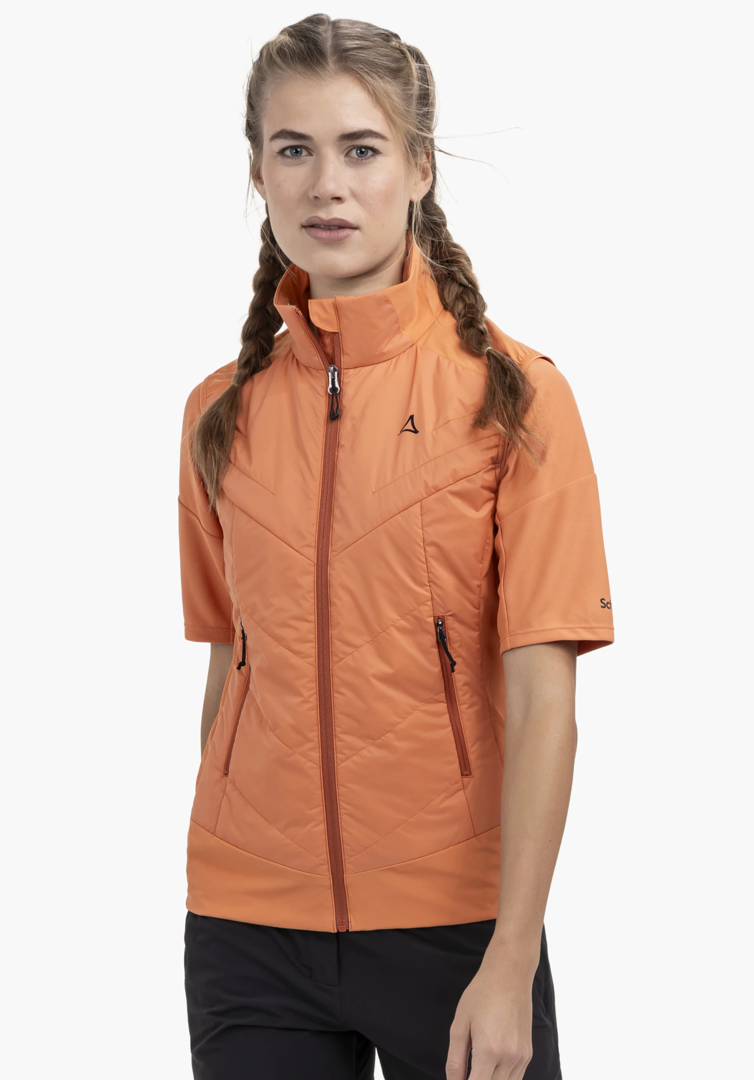 Hybrid Vt Style Blaueis WMS porté par un mannequin regardant l'appareil photo de face. La veste à manches courtes orange présente une fermeture éclair intégrale et un Schöffel-Logo visible sur la poitrine gauche. Le mannequin se tient debout devant un fond neutre.
