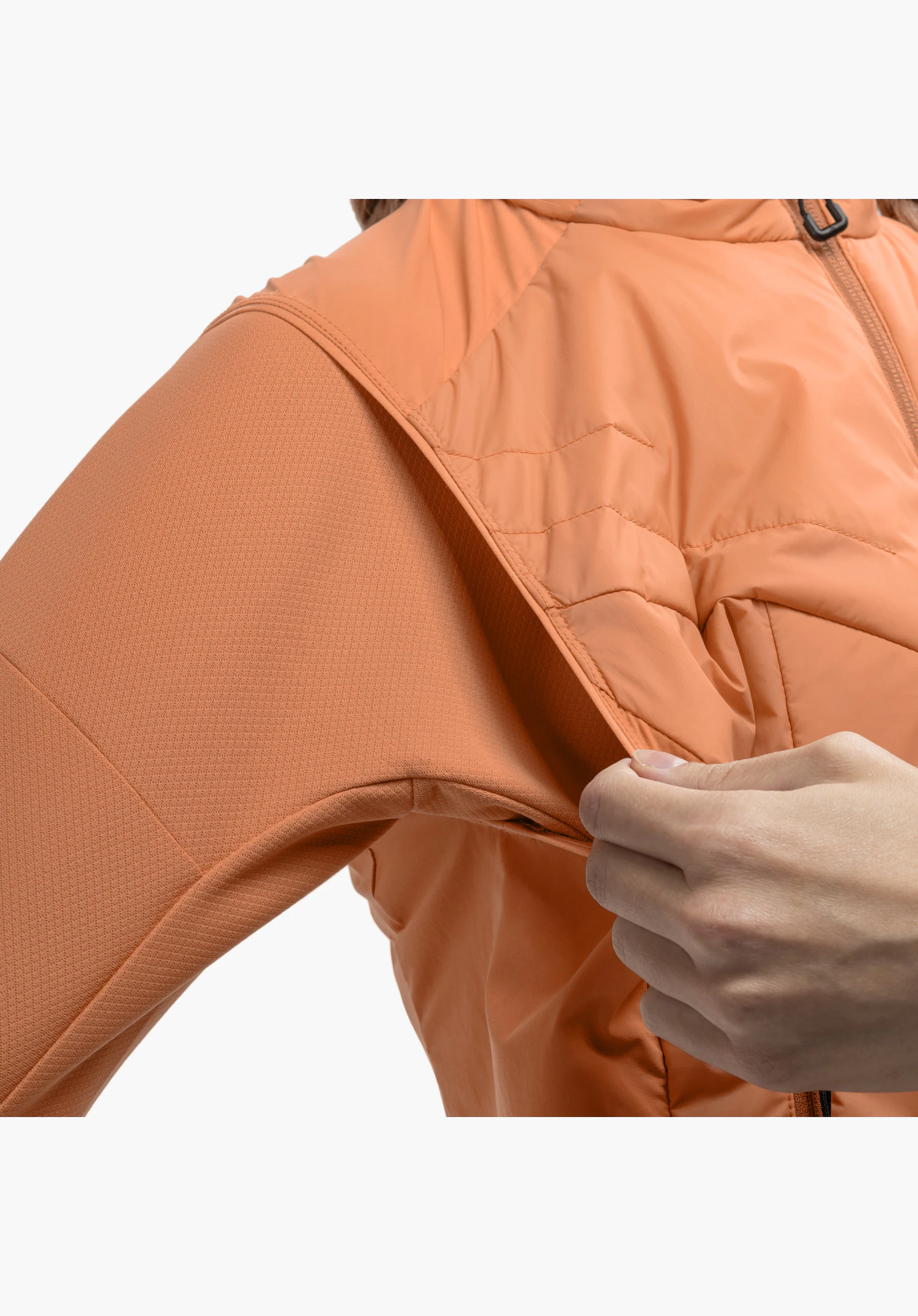 Hybrid Vt Style Blaueis WMS montre le détail du mélange de matières orange, où une main soulève le tissu lisse et matelassé du torse, exposant la surface texturée de la manche, en gros plan sur fond blanc.