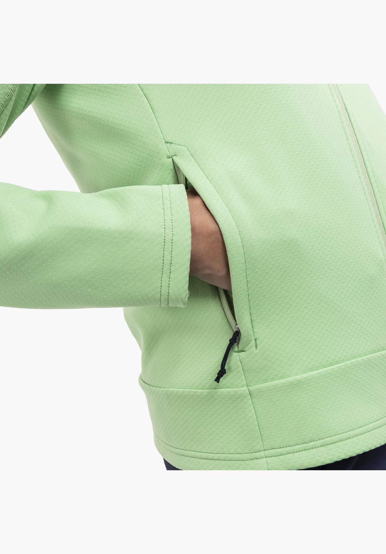Fleece Jk Style Uriezzo WMS, detail of the green side pocket with a black zip pull and a hand resting inside, showing the fine texture of the fleece fabric, close-up against a white background.