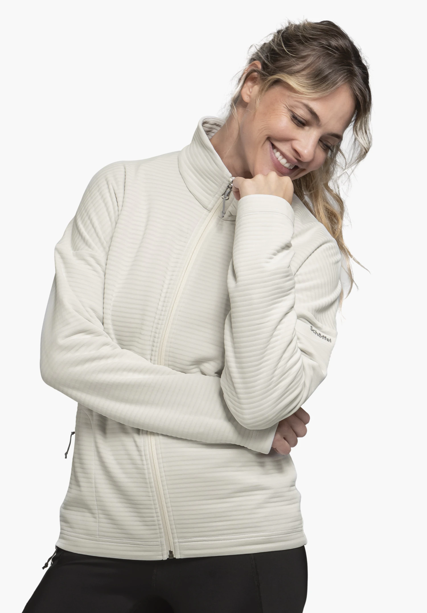 CIRC Fleece Jk Style Smue WMS, getragen von einem lächelnden Model, das leicht seitlich steht. Die Fleecejacke in der Farbe natur zeigt eine feine Rippenstruktur sowie das Schöffel-Logo auf dem linken Ärmel und wird vor einem neutralen Hintergrund präsentiert.