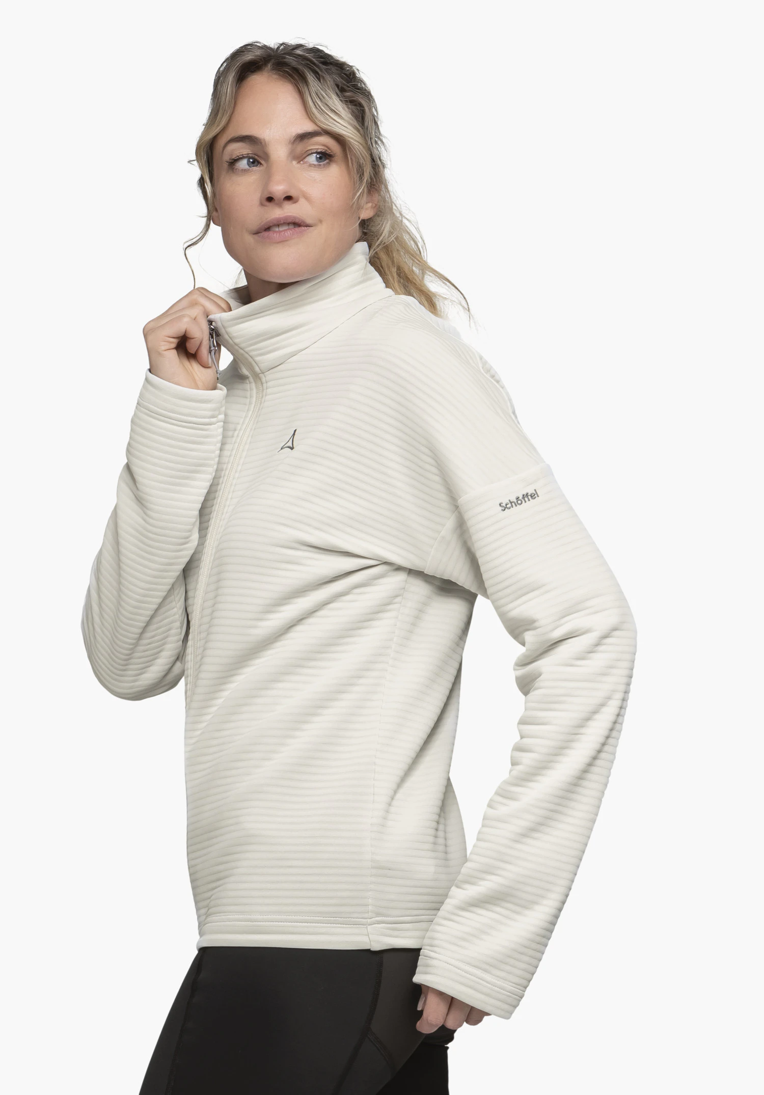 CIRC Fleece Jk Style Smue WMS in de kleur natur: Het model staat lichtjes zijwaarts voor een neutrale achtergrond en trekt de rits van het fleecejack omhoog. Het subtiele Schöffel-logo is zichtbaar op zowel de borst als de bovenarm.