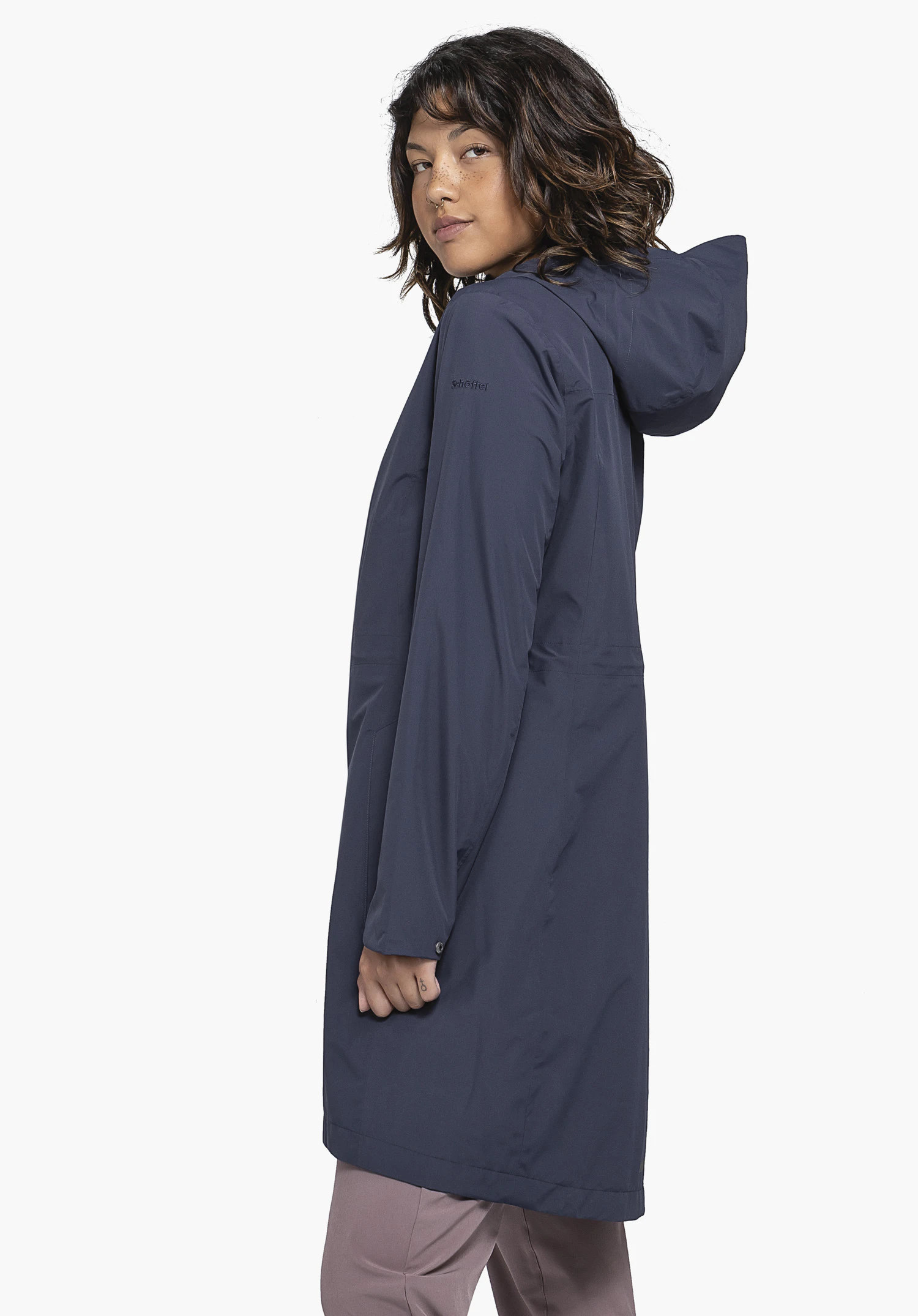 Coat Style Bohorok WMS in blue. The model is standing in a side profile against a neutral background, looking towards the camera. The coat features a simple blue design with the Schöffel logo subtly visible on the sleeve.