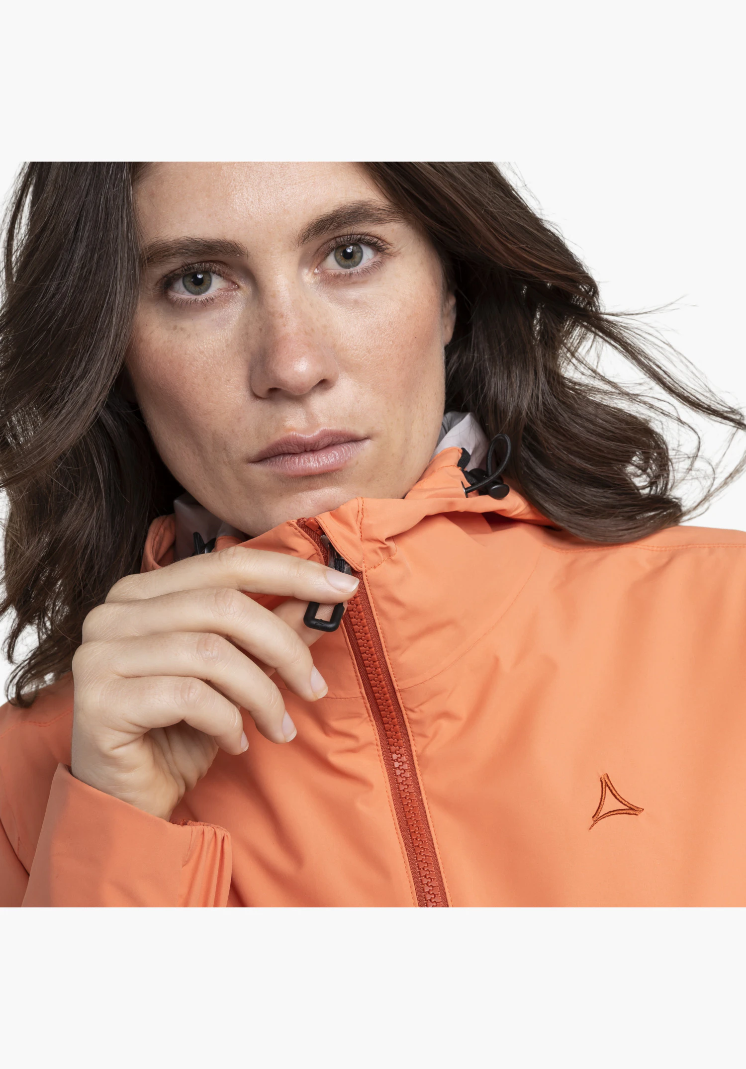 Jacket Style Bohorok WMS, detailed view of the zip being held by a hand, alongside the subtly embroidered Schöffel-Logo on the orange fabric. Close-up against a white/neutral background.