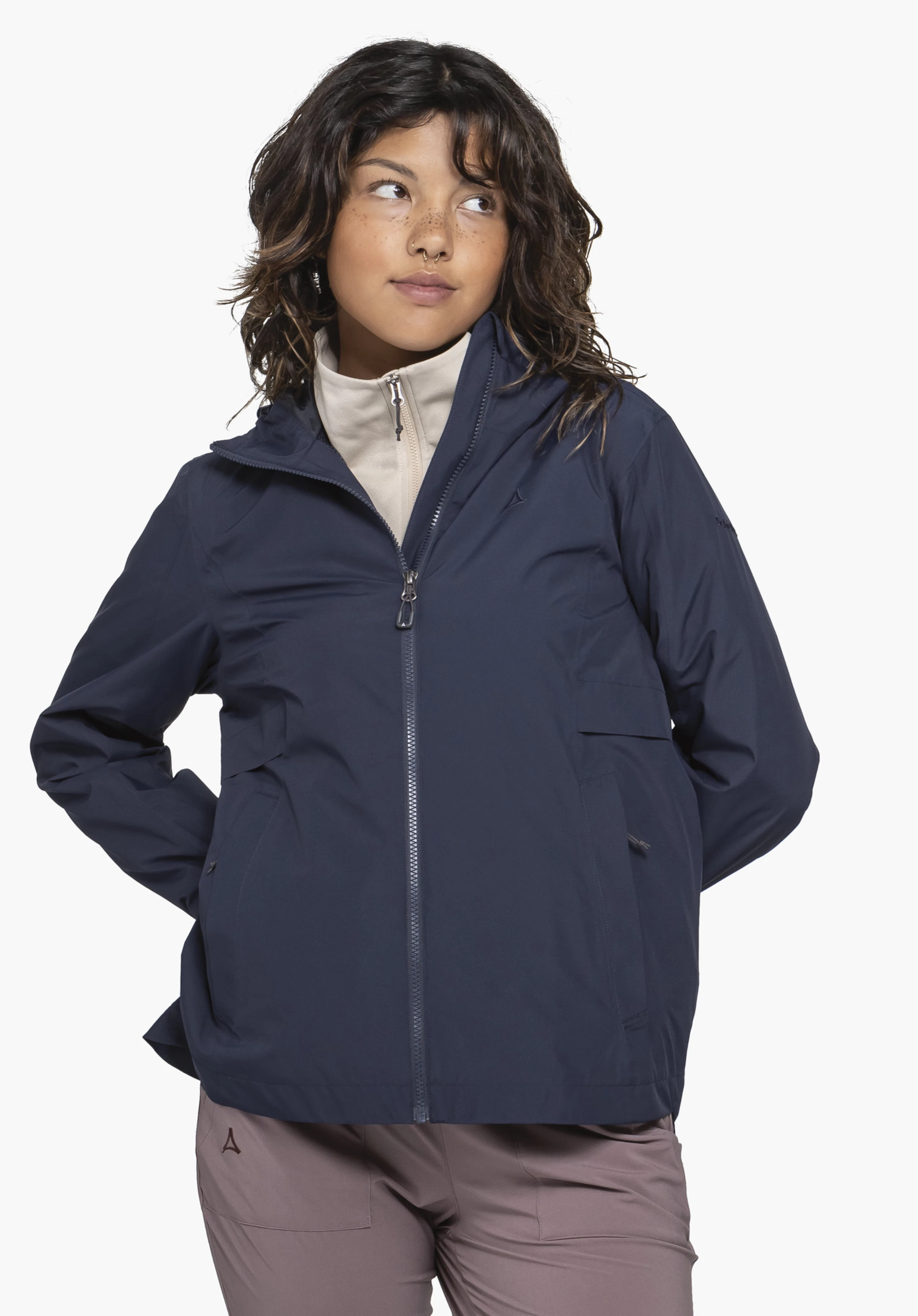 Jacket Style Bohorok WMS in het blauw. Een jonge vrouw staat frontaal voor een neutrale achtergrond en presenteert het blauwe jack met haar handen achter haar rug. Het subtiel geplaatste Schöffel-logo is zichtbaar op de borst.