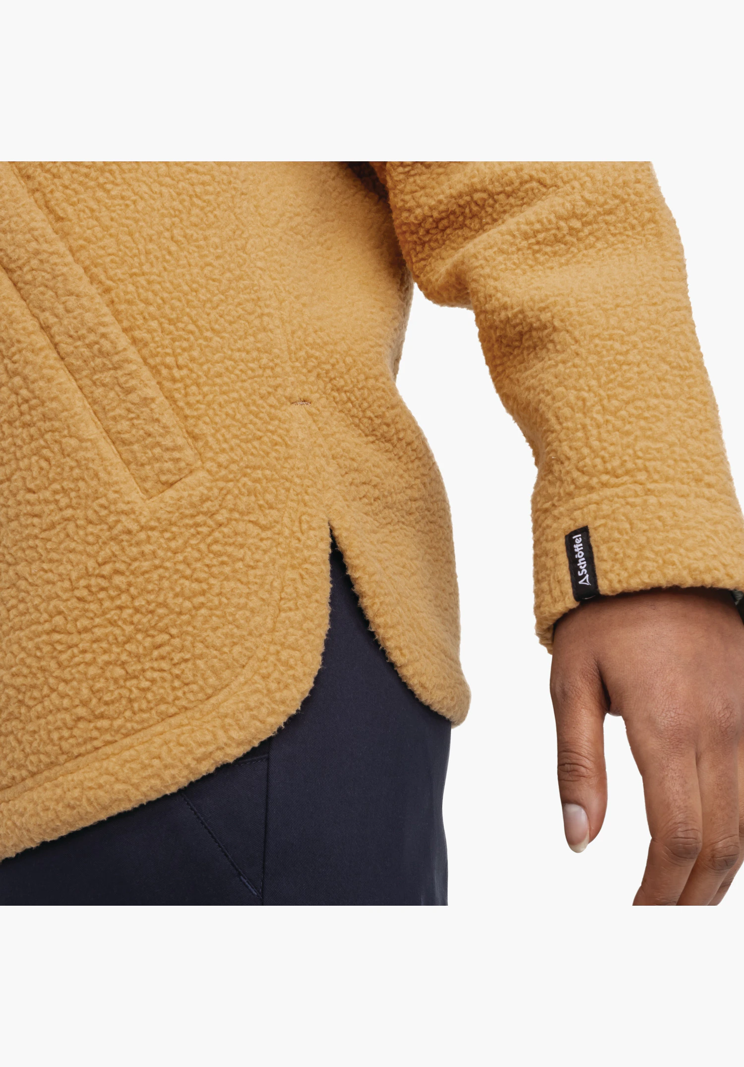 CIRC Fleece Jk Style Purga WMS zeigt den weichen, braunen Teddy-Fleece am abgerundeten Saum mit Seitenschlitz sowie das kleine Schöffel-Logo Label am Ärmelbund. Nahaufnahme vor weißem/neutralem Hintergrund.