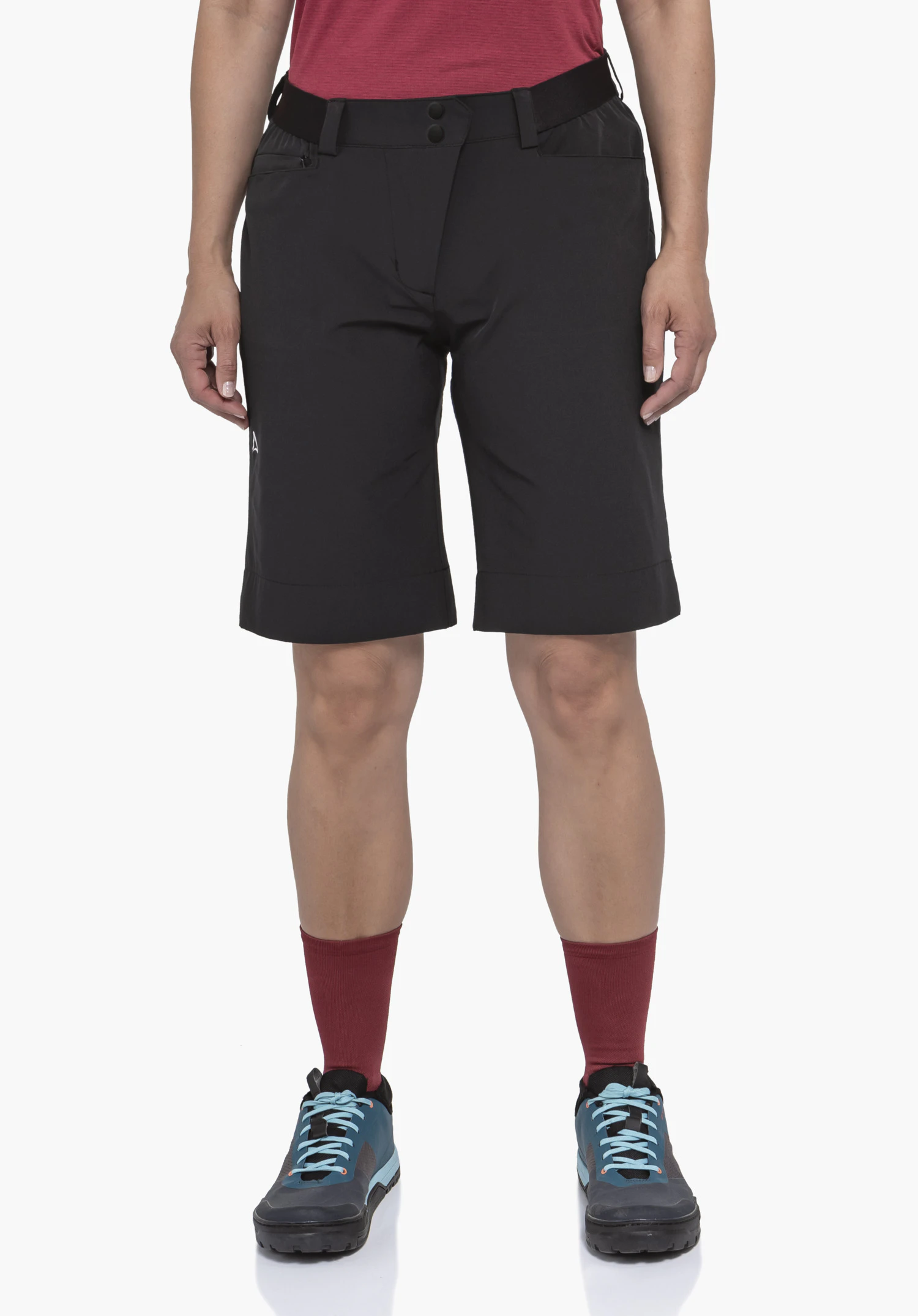 Shorts Style Keitele WMS black shorts with Schöffel logo, worn standing against a white background; red shirt, red socks and blue and light blue shoes visible.