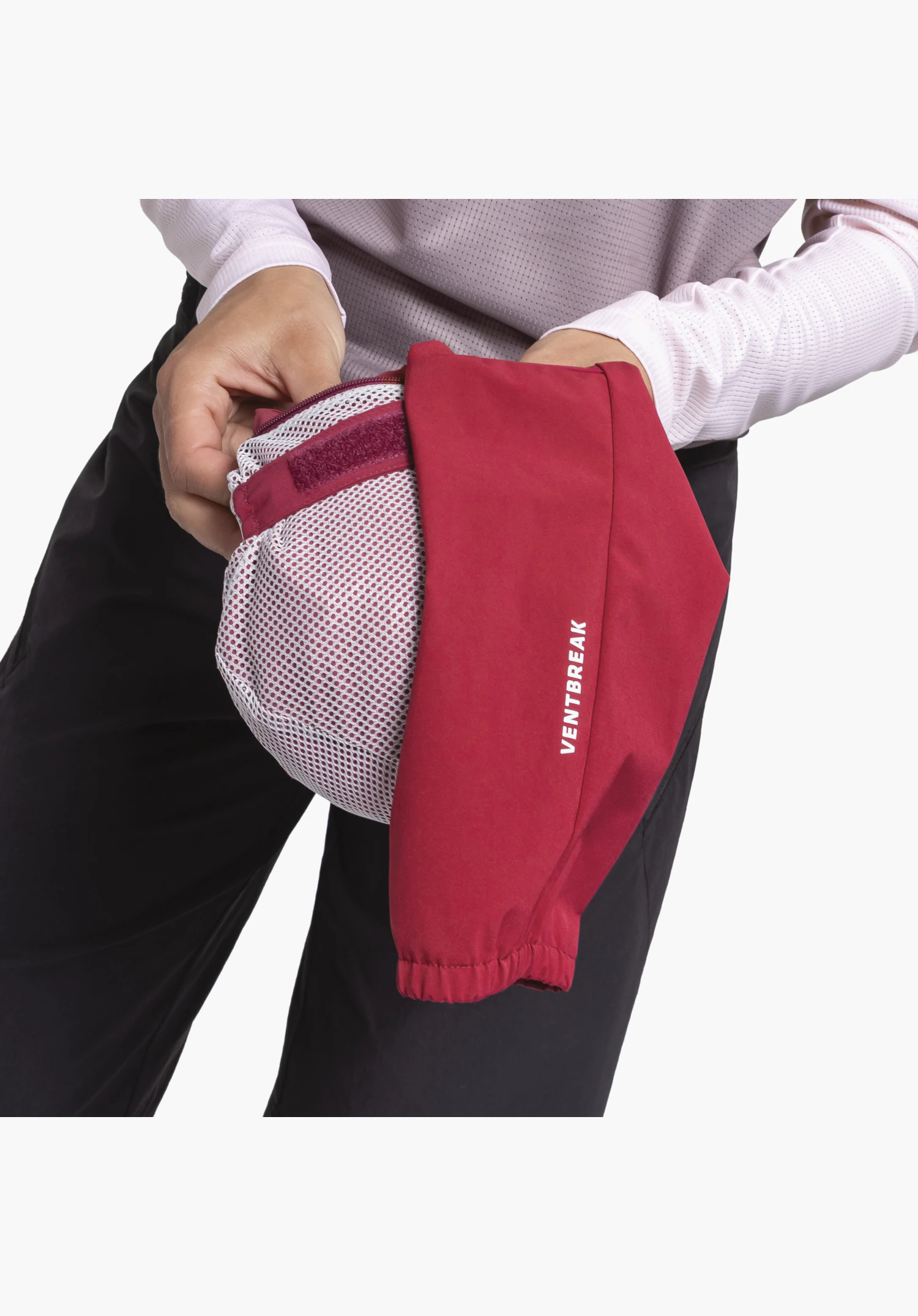 Hybrid Jk Style Mamry WMS, detail view of the pack-away function with a white mesh pocket into which the red fabric featuring a white "VENTBREAK" print and velcro fastening is partially packed, close-up against a white/neutral background.