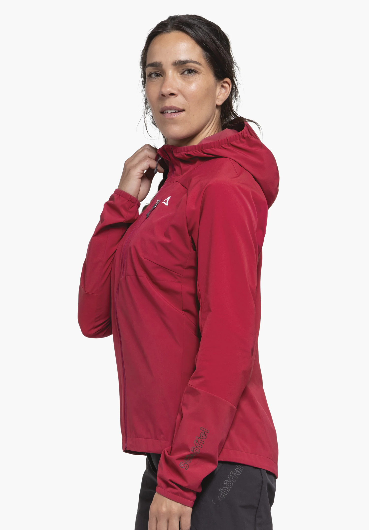 Hybrid Jk Style Mamry WMS in vibrant red against a neutral background. The athlete stands sideways to the camera, showcasing the jacket, with the white Schöffel logo visible on the chest and the subtle brand lettering on the sleeve.