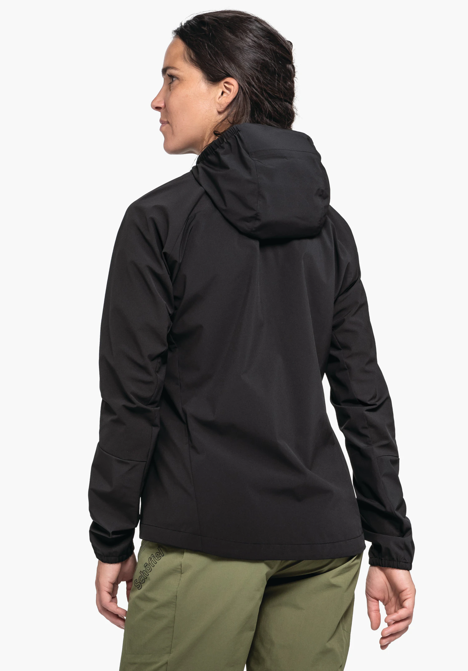 Hybrid Jk Style Mamry WMS in Schwarz. Ein Model präsentiert die Jacke mit Kapuze in der Rückenansicht vor einem neutralen Hintergrund. Kombiniert wird die Jacke mit einer grünen Hose, auf der das Schöffel-Logo sichtbar ist.