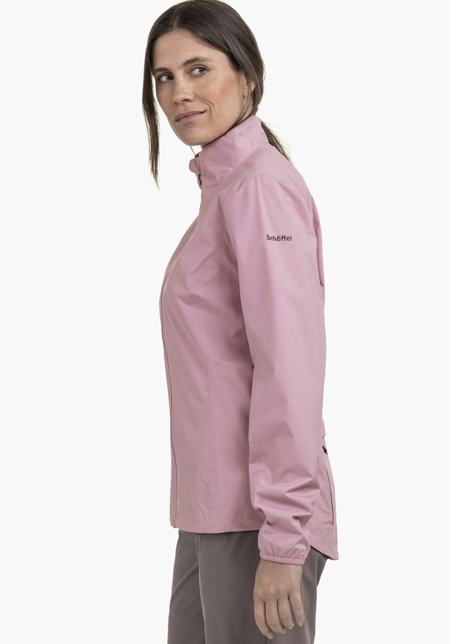 Jacket Style Lurbek WMS: Een vrouw draagt het sportieve jack in roze en staat zijwaarts voor een neutrale achtergrond. Ze kijkt recht in de camera, terwijl het Schöffel-logo subtiel op de bovenarm zichtbaar is.