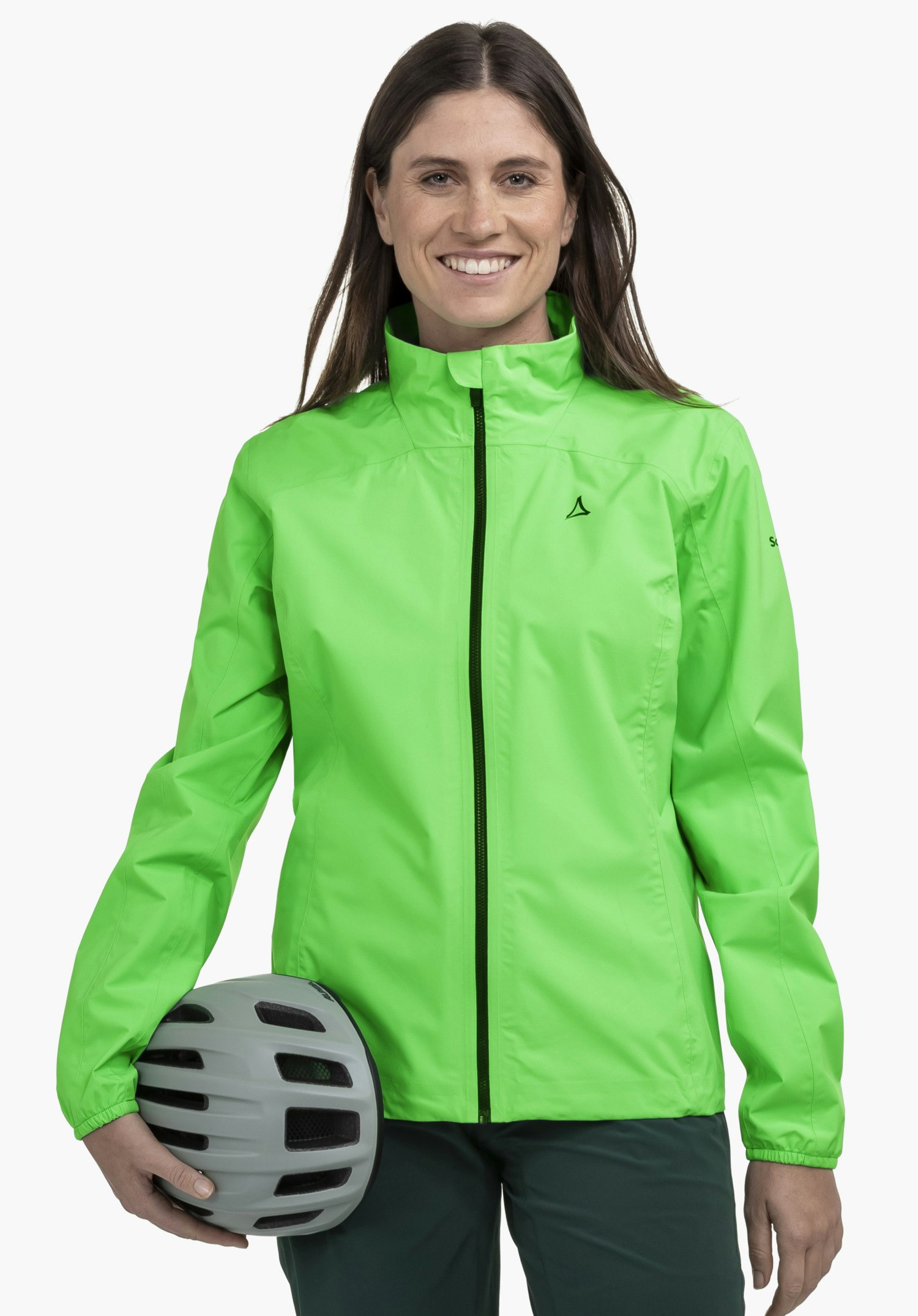 Jacket Style Lurbek WMS an einem Model, das frontal steht und in die Kamera lächelt. Sie trägt die grüne Jacke mit dem sichtbaren Schöffel-Logo auf der linken Brust und hält einen Fahrradhelm im rechten Arm vor einem neutralen Hintergrund.