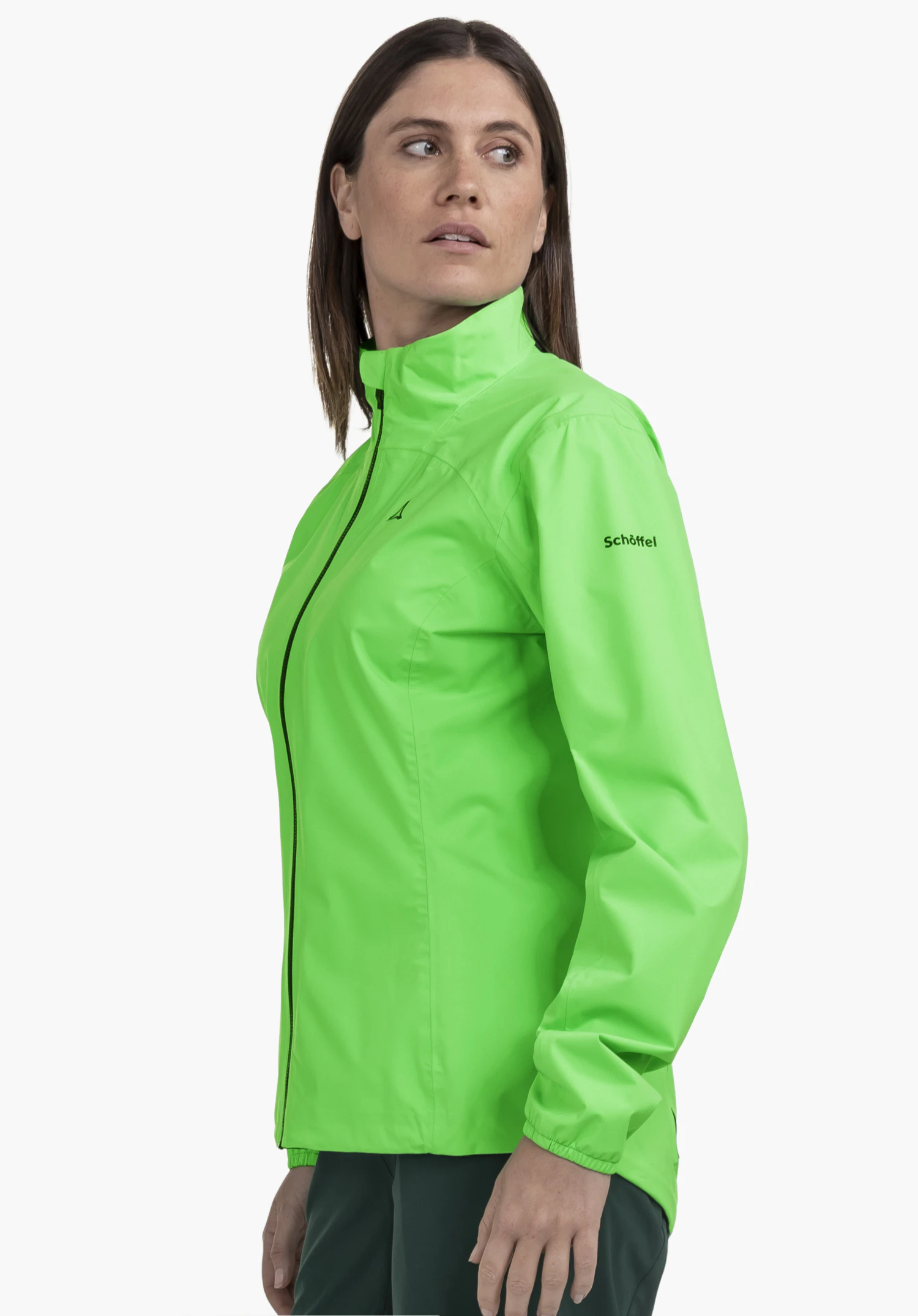 Jacket Style Lurbek WMS : Une femme portant la veste vert vif se tient de profil devant un fond neutre et regarde par-dessus son épaule, tandis que le discret logo Schöffel sur le haut du bras ajoute une touche.