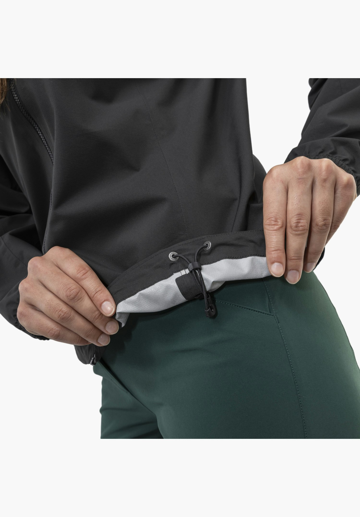Jacket Style Lurbek WMS zeigt den verstellbaren, schwarzen Saum mit elastischem Kordelzug, Kordelstopper und hellem Innenfutter, der von zwei Händen gehalten wird. Nahaufnahme vor weißem/neutralem Hintergrund.