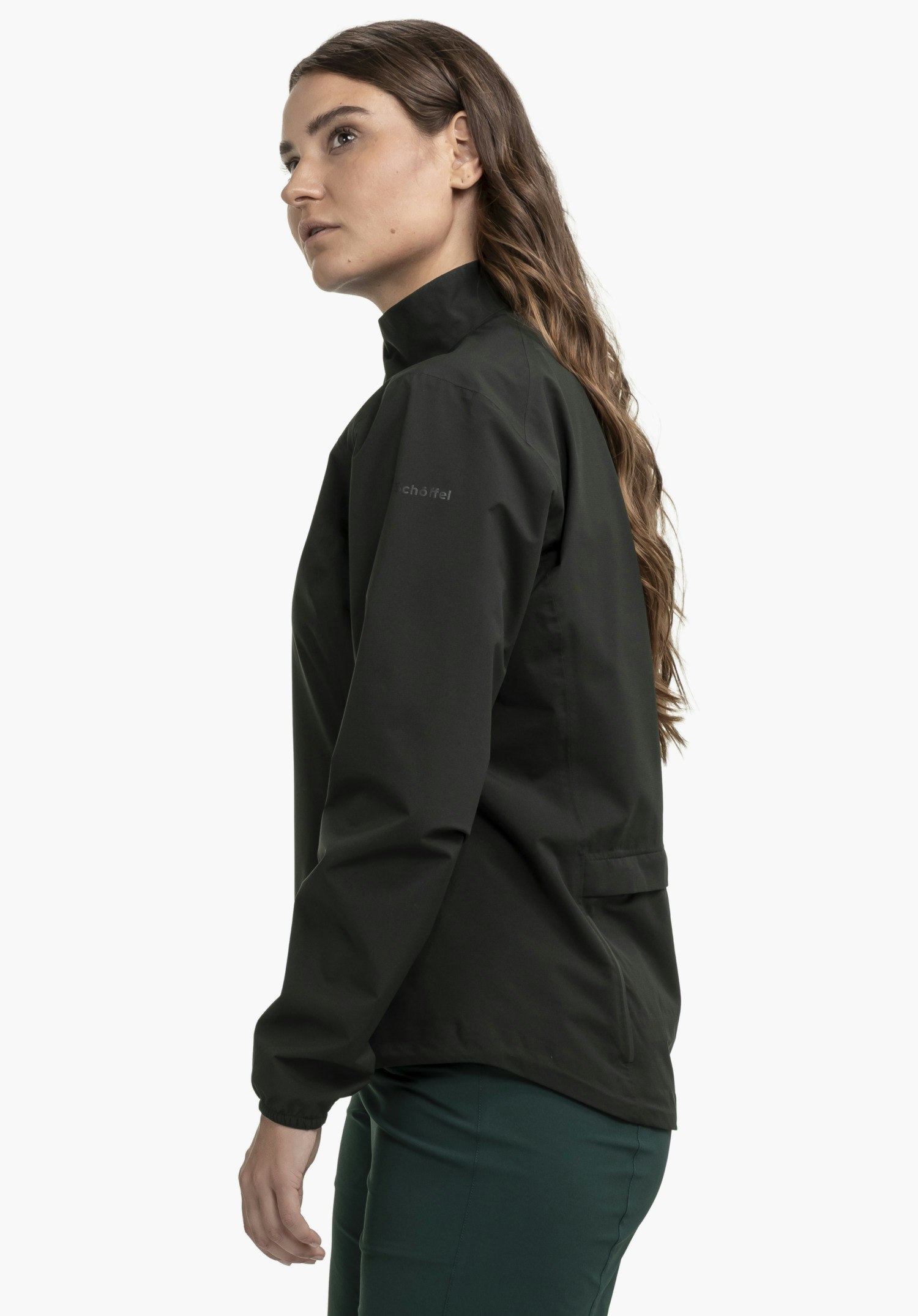 Jacket Style Lurbek WMS in zeitlosem Schwarz. Die Trägerin steht seitlich vor einem neutralen Hintergrund und präsentiert die Jacke in einer klaren Seitenansicht. Das dezent platzierte Schöffel-Logo auf dem Oberarm ist gut erkennbar.