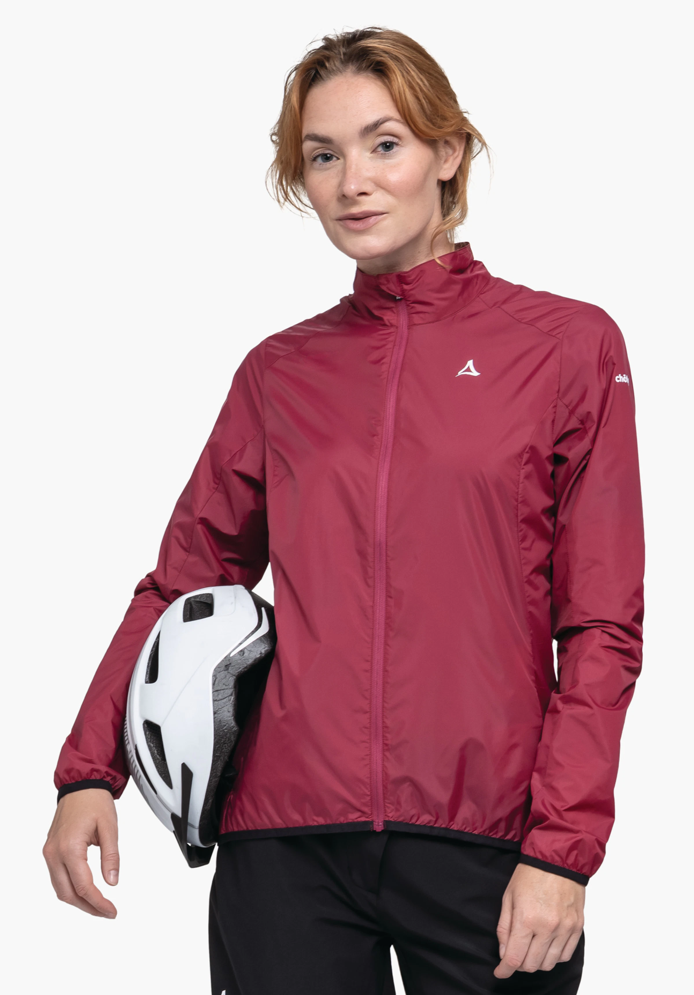Jacket Style Cannobio WMS dunkelrote Jacke mit Schöffel-Logo; Modell trägt sie, hält einen weißen Fahrradhelm seitlich an der Hüfte, steht vor weißem Hintergrund und trägt schwarze Hosen.
