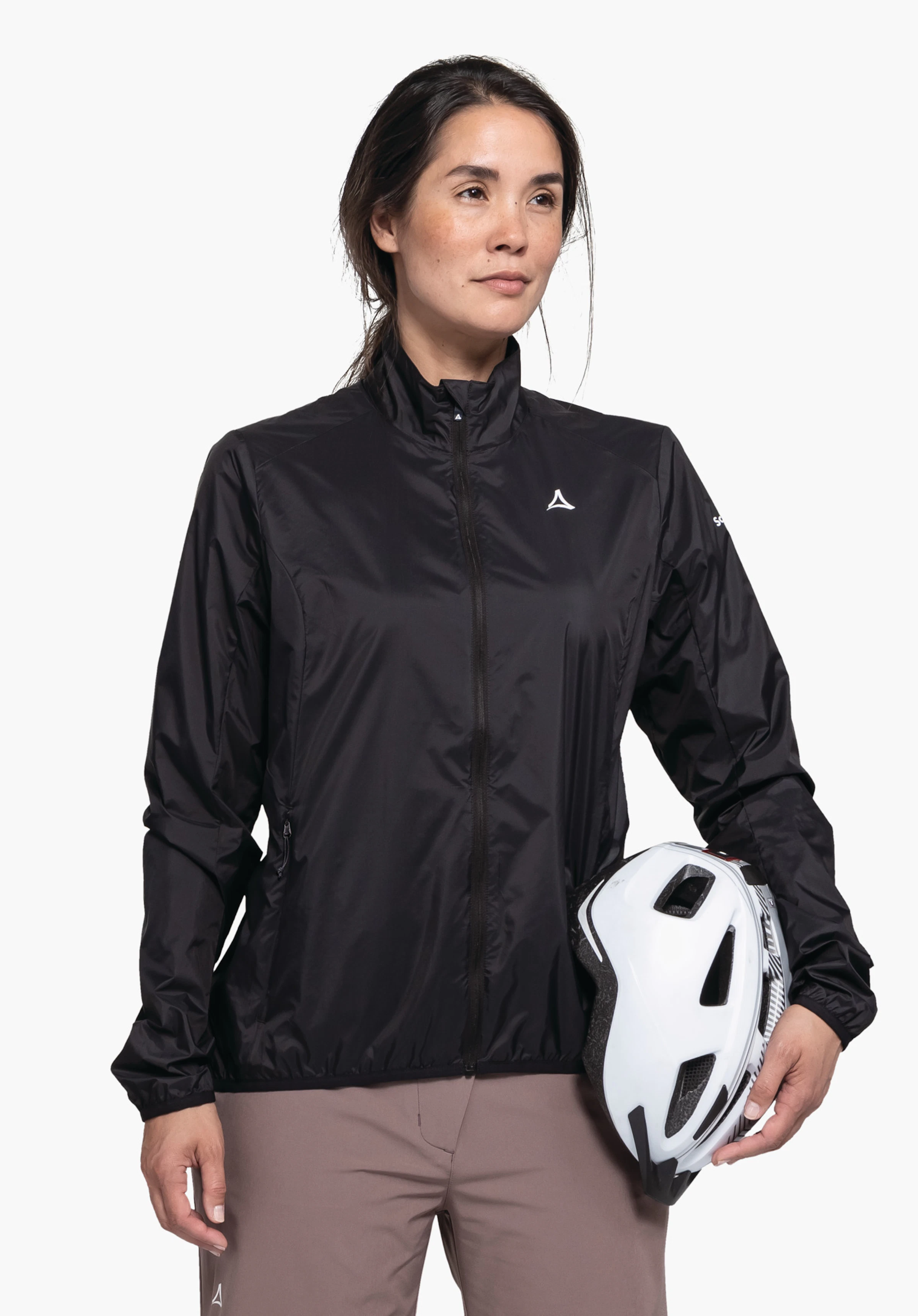Jacket Style Cannobio WMS getragen von einem Model in Frontalansicht, das einen weißen Fahrradhelm unter dem linken Arm hält. Die schwarze Jacke zeigt deutlich das weiße Schöffel-Logo auf der linken Brust, fotografiert vor einem neutralen Hintergrund.