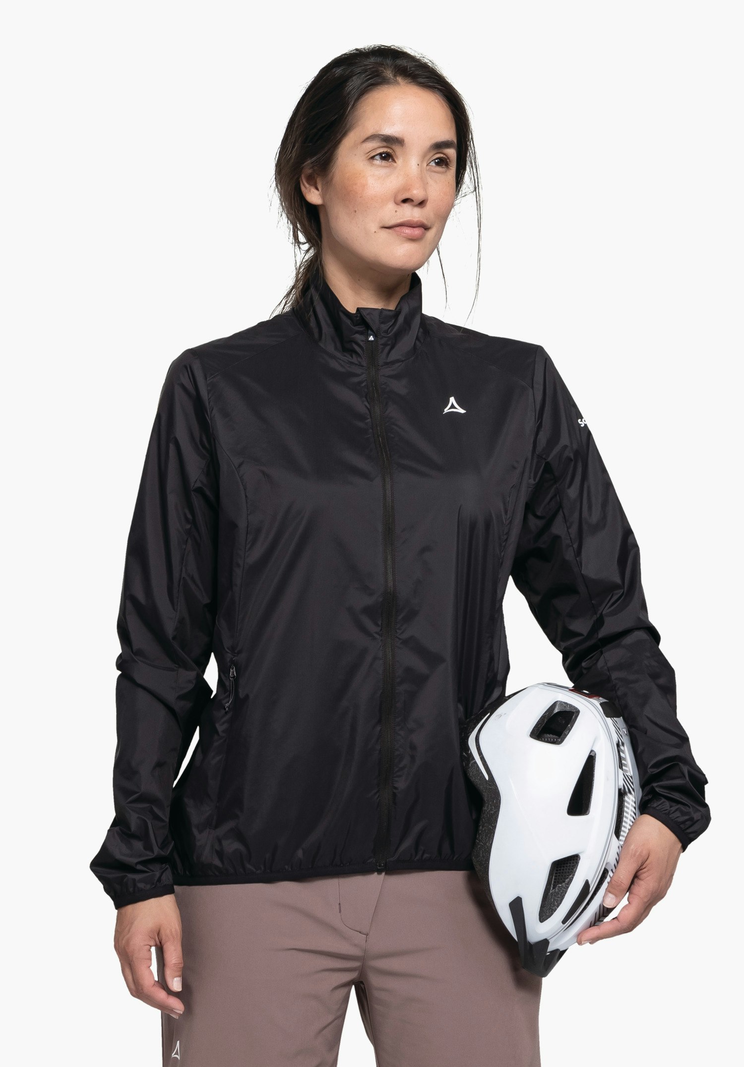 Jacket Style Cannobio WMS worn by a model standing in a frontal pose, holding a white bicycle helmet under her left arm. The black jacket clearly shows the white Schöffel logo on the left chest, photographed against a neutral background.