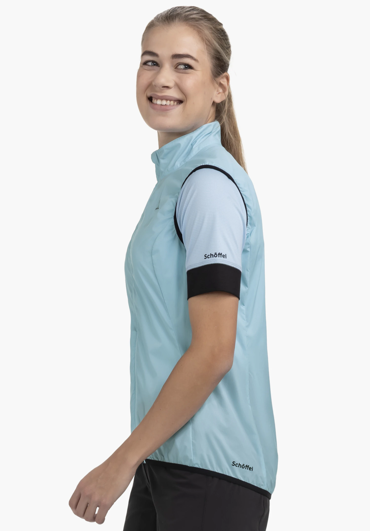 Vest Style Cannobio WMS in blue, captured in a side-profile shot against a neutral background. The model is smiling, with the Schöffel logo visible at the hem of the vest.