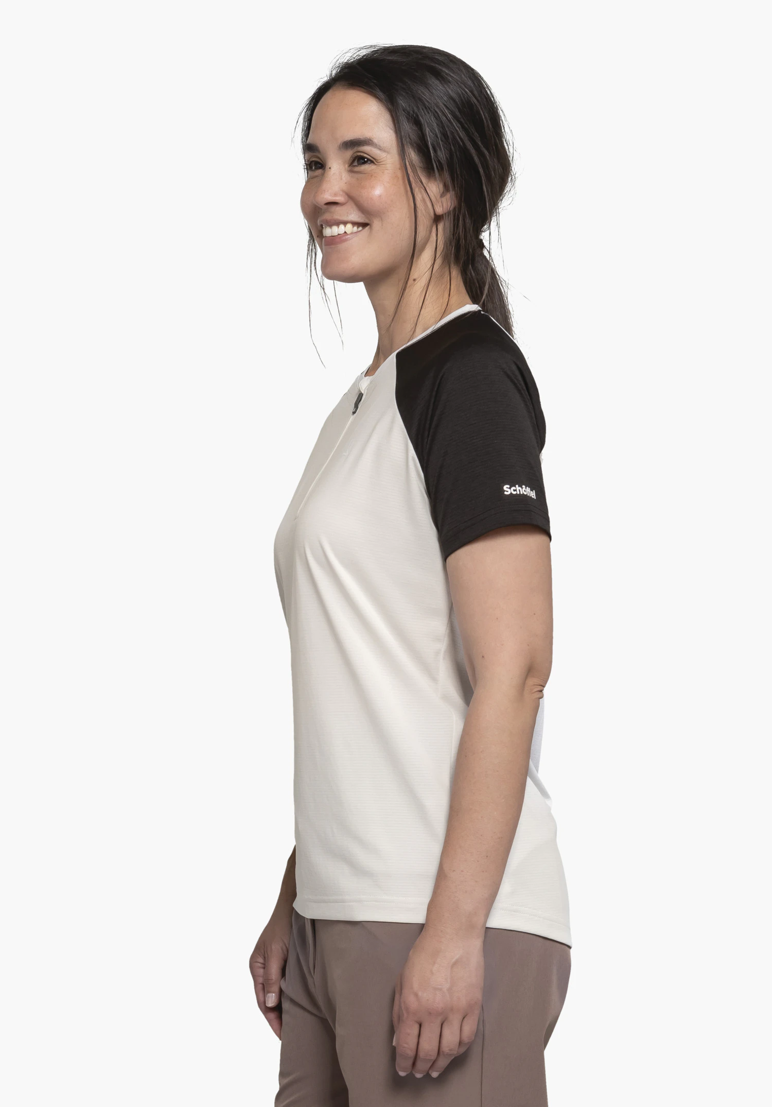 CIRC Shirt Style Wetluga WMS dans le coloris natur. Une femme souriante pose de profil sur un fond neutre et présente le haut doté de manches noires contrastantes et du logo Schöffel bien visible sur l'épaule.