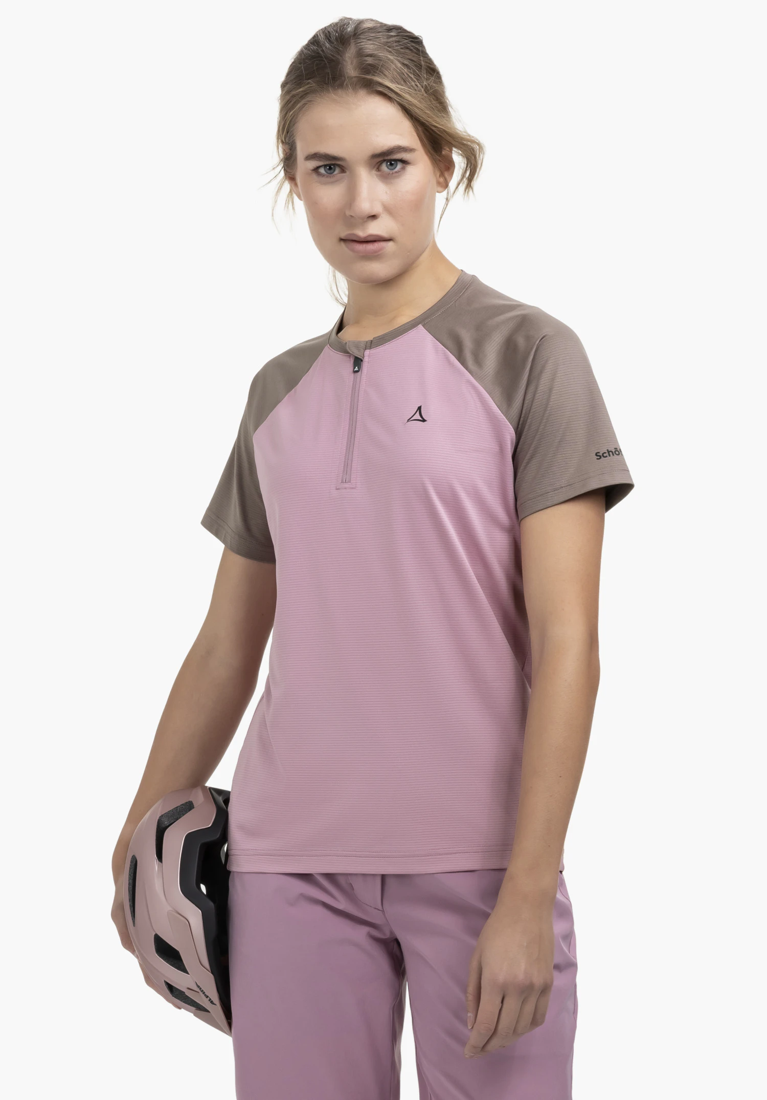 CIRC Shirt Style Wetluga WMS en rose. Le mannequin est présenté de face sur un fond neutre et porte le t-shirt à demi-zip, qui séduit par son design bicolore. Le discret logo Schöffel sur la poitrine et la manche souligne le look sportif, tandis que le mannequin tient un casque assorti à la main.