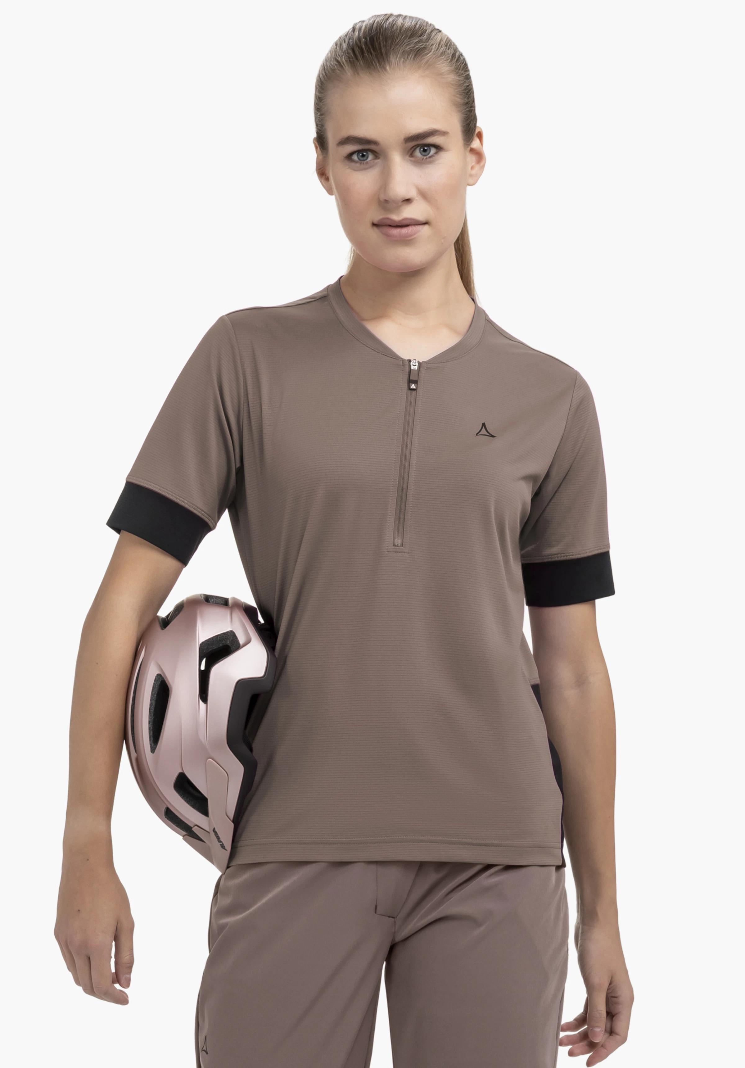 CIRC Shirt Style Pinega WMS: Das Model steht frontal vor einem neutralen Hintergrund und trägt das Shirt in Braun mit einem Fahrradhelm unter dem Arm. Das diskrete Schöffel-Logo ist gut auf der Brust zu sehen.