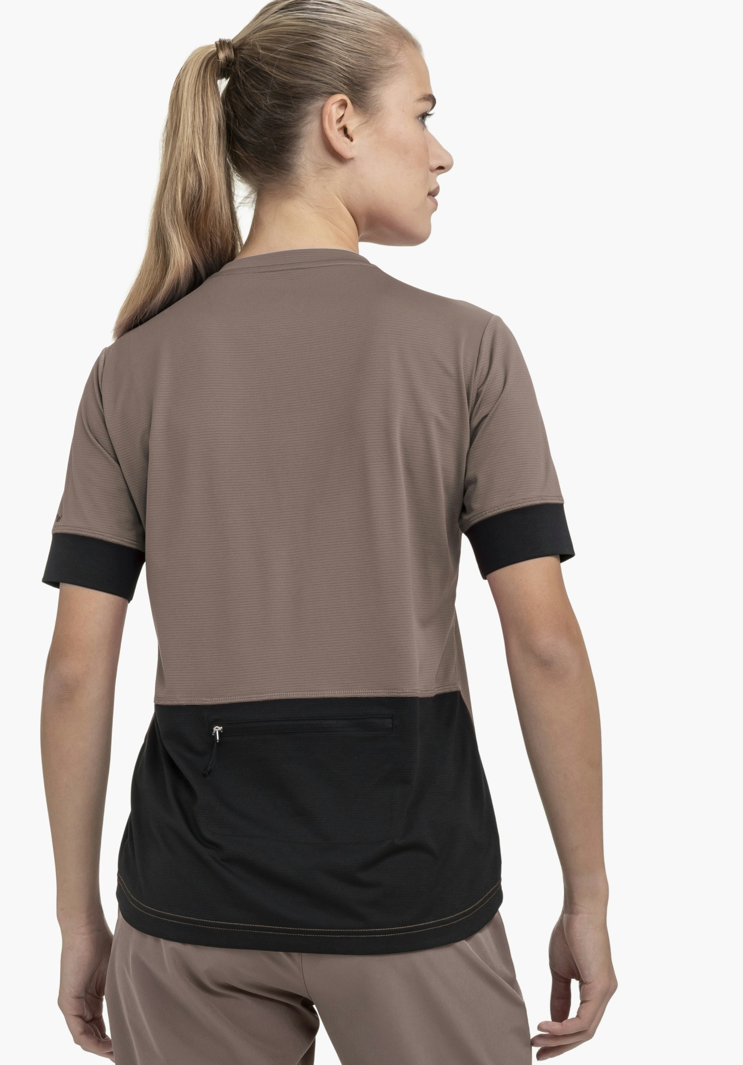 CIRC Shirt Style Pinega WMS : Une femme, vue de dos sur un fond neutre, porte ce t-shirt fonctionnel de couleur marron. Le modèle met en évidence la poche zippée pratique dans le dos ainsi que le logo Schöffel discret sur la manche.