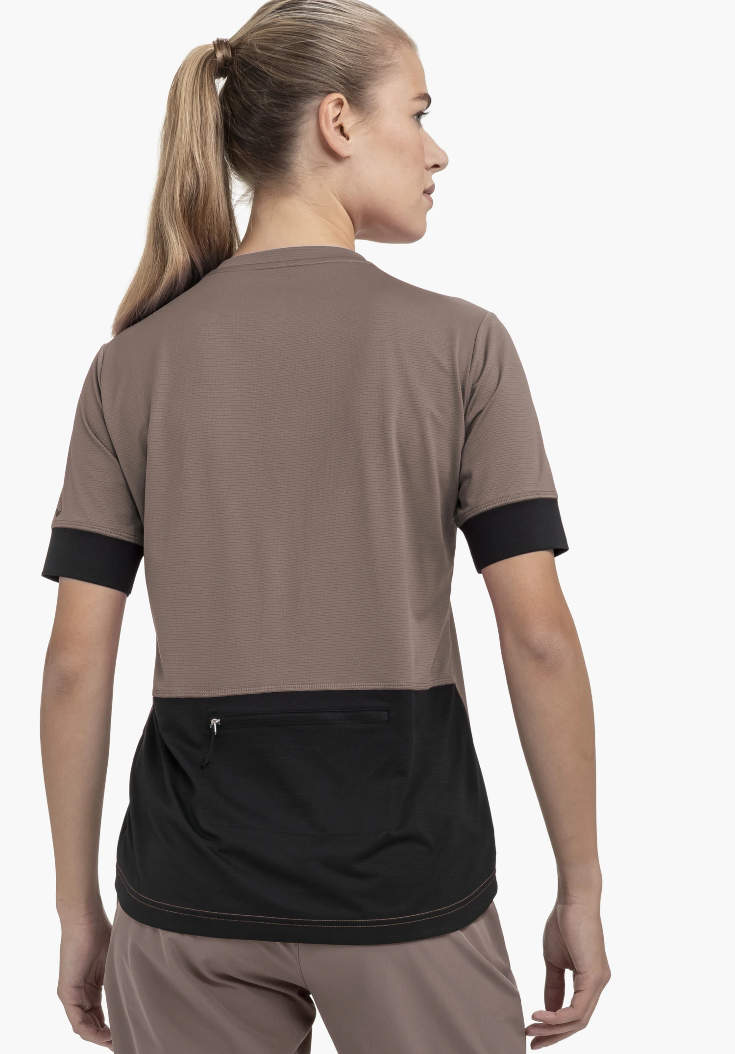 CIRC Shirt Style Pinega WMS : Une femme, vue de dos sur un fond neutre, porte ce t-shirt fonctionnel de couleur marron. Le modèle met en évidence la poche zippée pratique dans le dos ainsi que le logo Schöffel discret sur la manche.