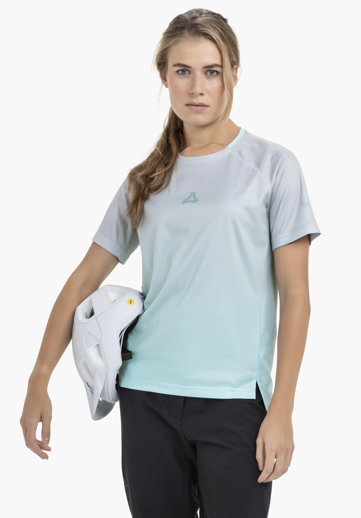 Shirt Style Koitere WMN in Blau: Das Model steht frontal vor einem neutralen Hintergrund und trägt das Shirt mit dem gut sichtbaren Schöffel-Logo auf der Brust. Sie hält einen Fahrradhelm in der Hand, was den sportlichen Charakter des Outfits unterstreicht.
